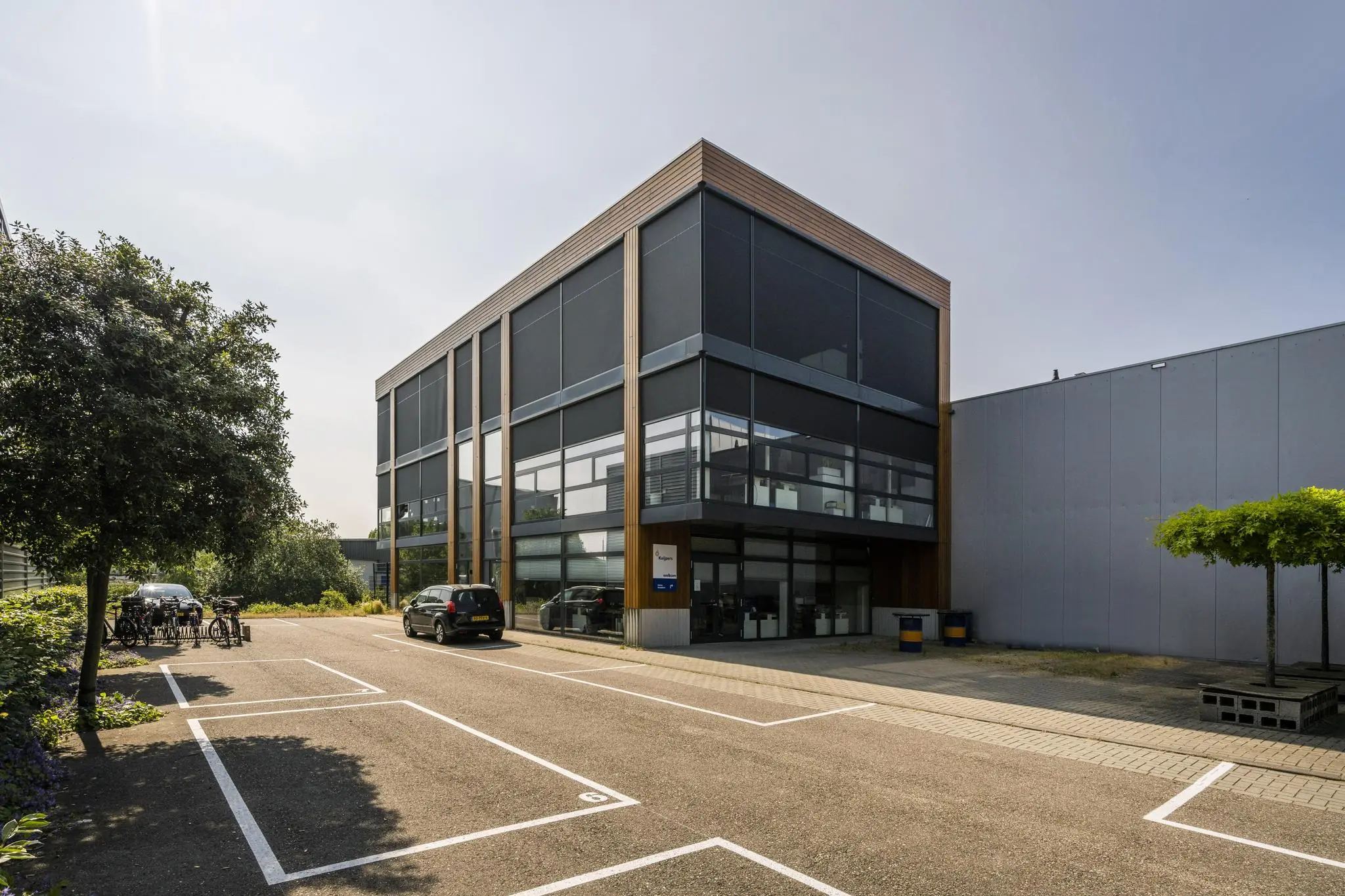 Modern kantoorgebouw aan de Asterweg met grote ramen en een deels lege parkeerplaats op de voorgrond.