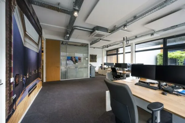 Modern kantoorinterieur aan de Asterweg met bureaus, computers, glazen vergaderruimte en grote kunstafbeelding op de muur.