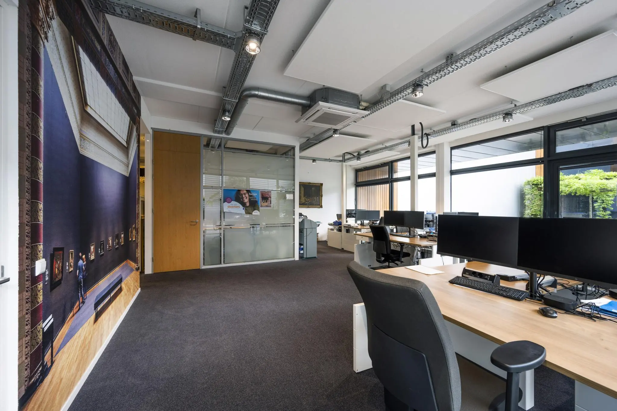 Modern kantoorinterieur aan de Asterweg met bureaus, computers, glazen vergaderruimte en grote kunstafbeelding op de muur.