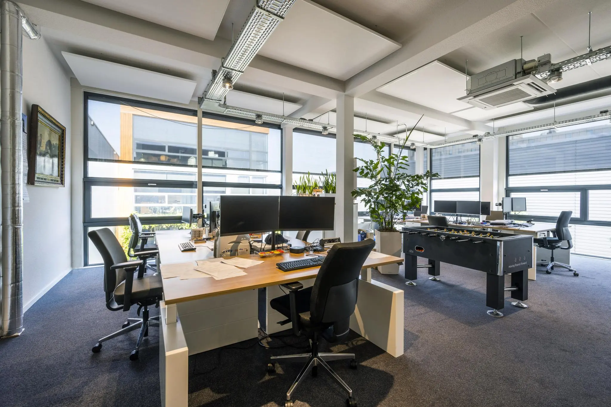 Modern kantoorinterieur op de Asterweg met bureaus, computers, grote ramen en een tafelvoetbaltafel.