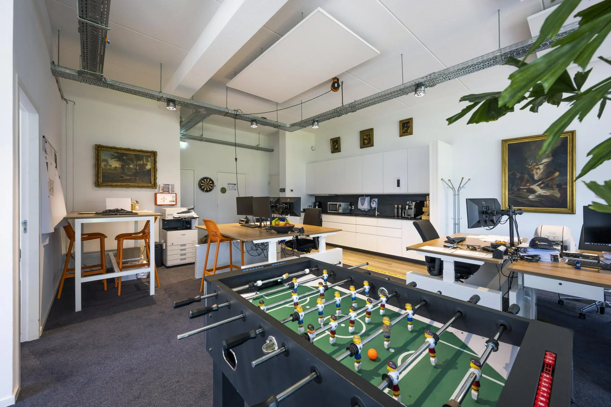 Moderne kantoorruimte aan de Asterweg met werkplekken, keuken, tafelvoetbaltafel en decoratieve schilderijen.