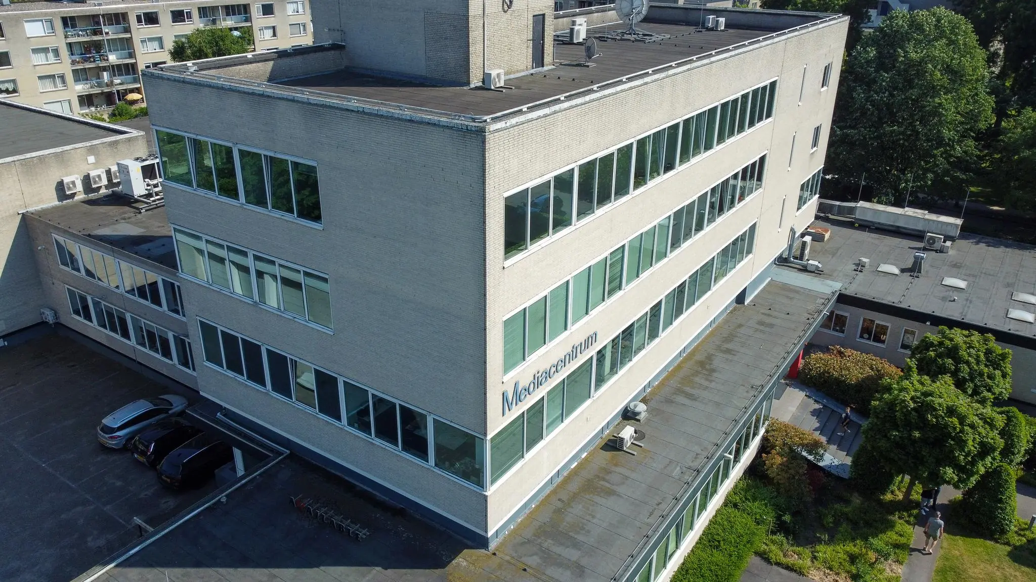 Luchtfoto van het Mediacentrum-gebouw aan de Hengeveldstraat met parkeerplaats en omliggend groen.