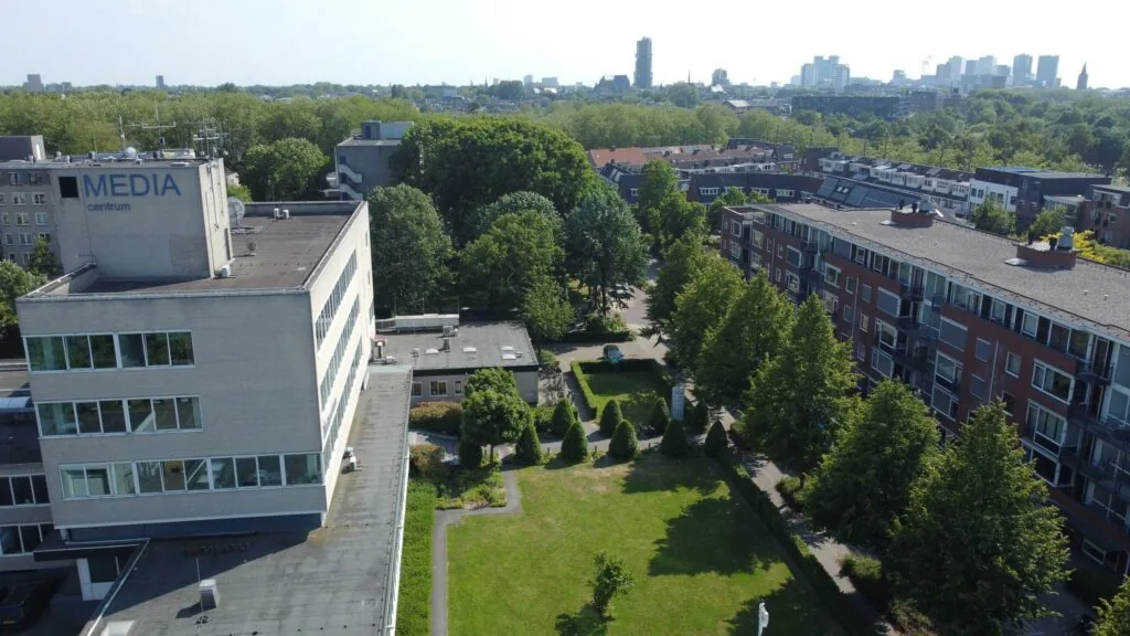 Luchtfoto van het Media Centrum aan de Hengeveldstraat met omliggende gebouwen, groenstrook en de skyline van Utrecht op de achtergrond.