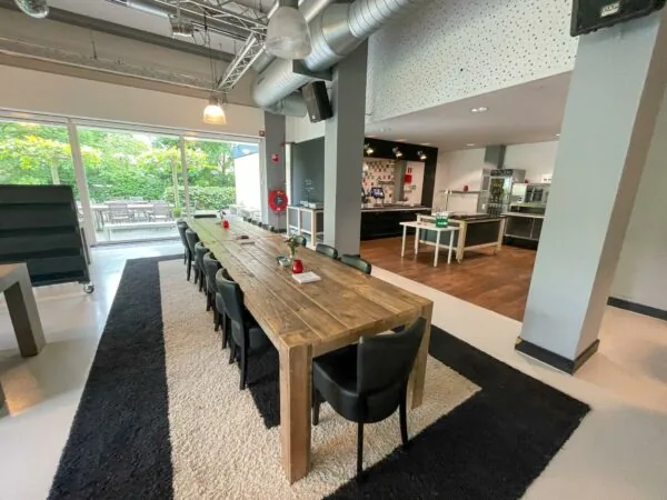 Gemeenschappelijke ruimte aan de Hengeveldstraat met lange houten eettafel, keuken en uitzicht op een terras met tuin.