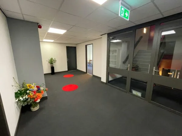 Moderne kantoorhal aan de Hengeveldstraat met bloemen, planten, rode vloercirkels en een trap achter glazen deuren.