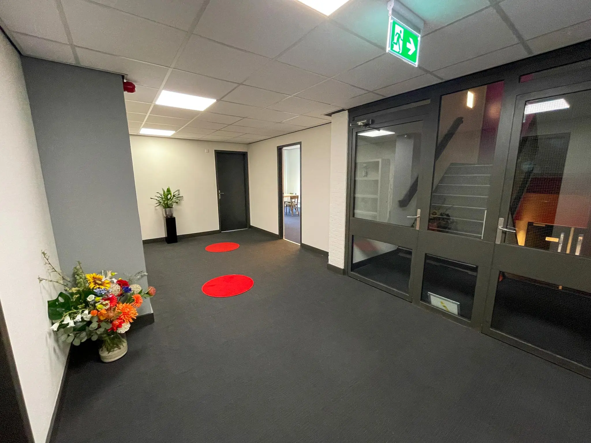 Moderne kantoorhal aan de Hengeveldstraat met bloemen, planten, rode vloercirkels en een trap achter glazen deuren.