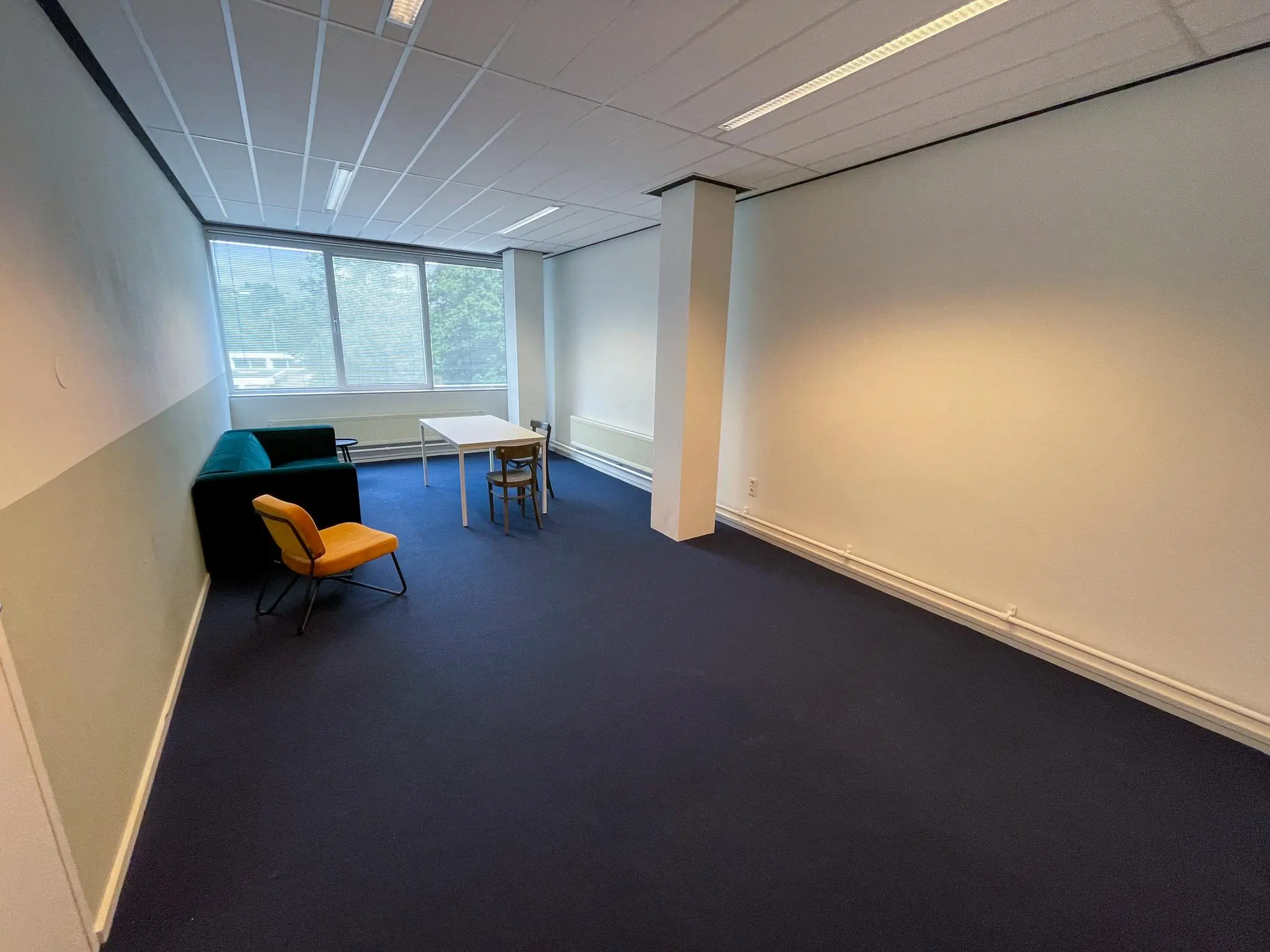 Kantoorruimte aan de Hengeveldstraat met enkele stoelen, een tafel en een bank bij een groot raam.