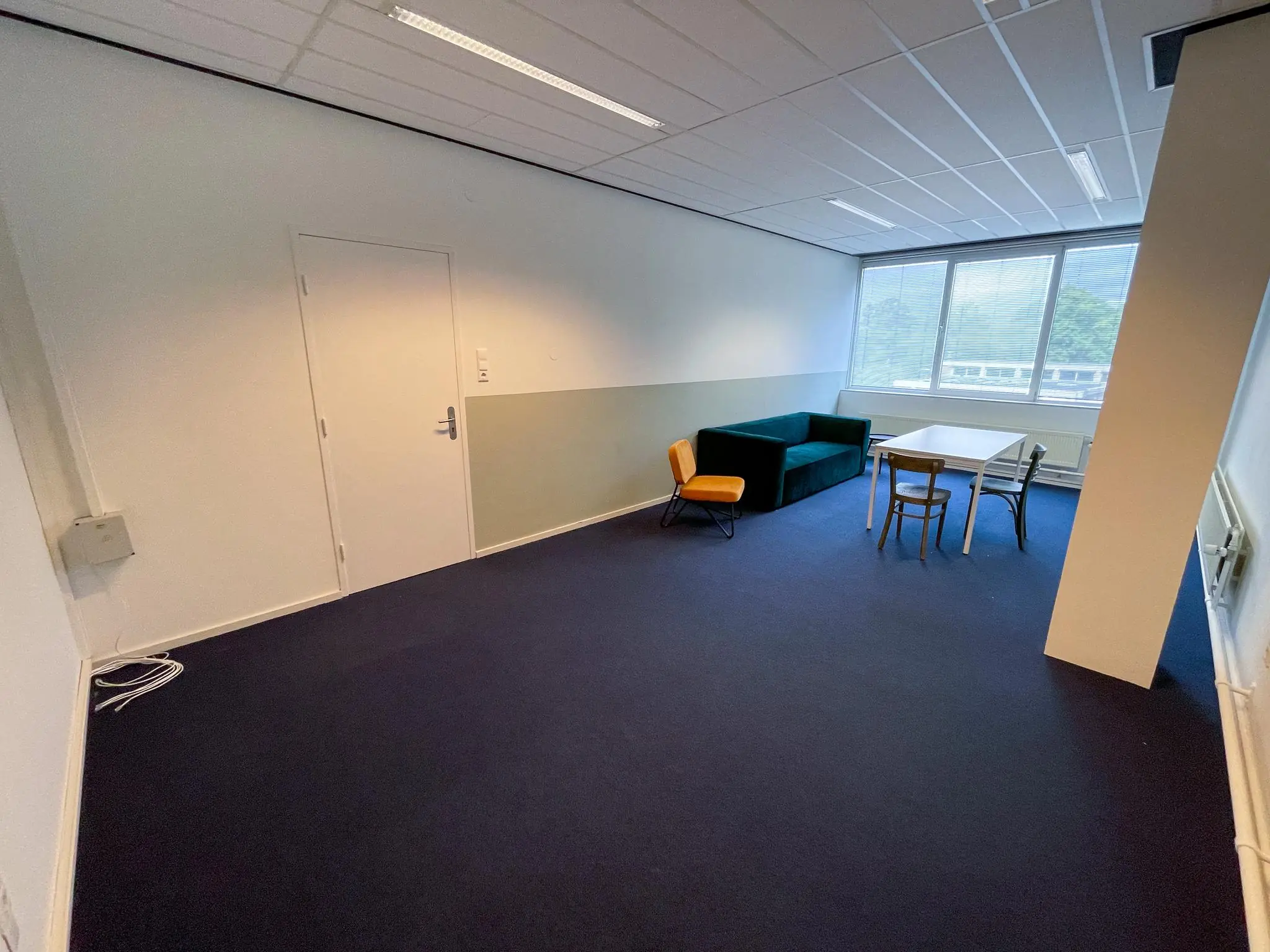 Kleine kantoorruimte aan de Hengeveldstraat met een tafel, stoelen en een groene bank bij het raam.
