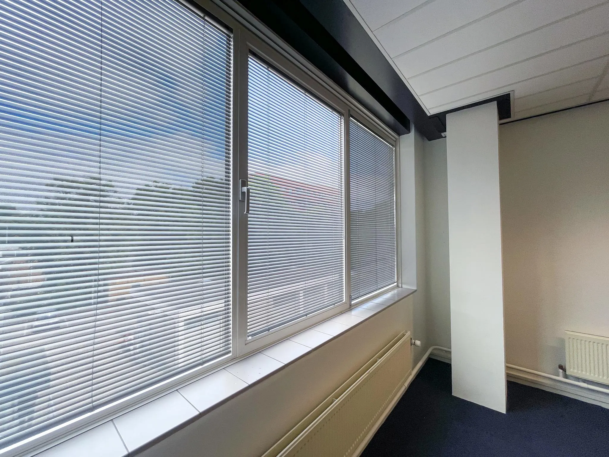 Kantoorruimte aan de Hengeveldstraat met grote ramen voorzien van jaloezieën en een radiator onder het raam.