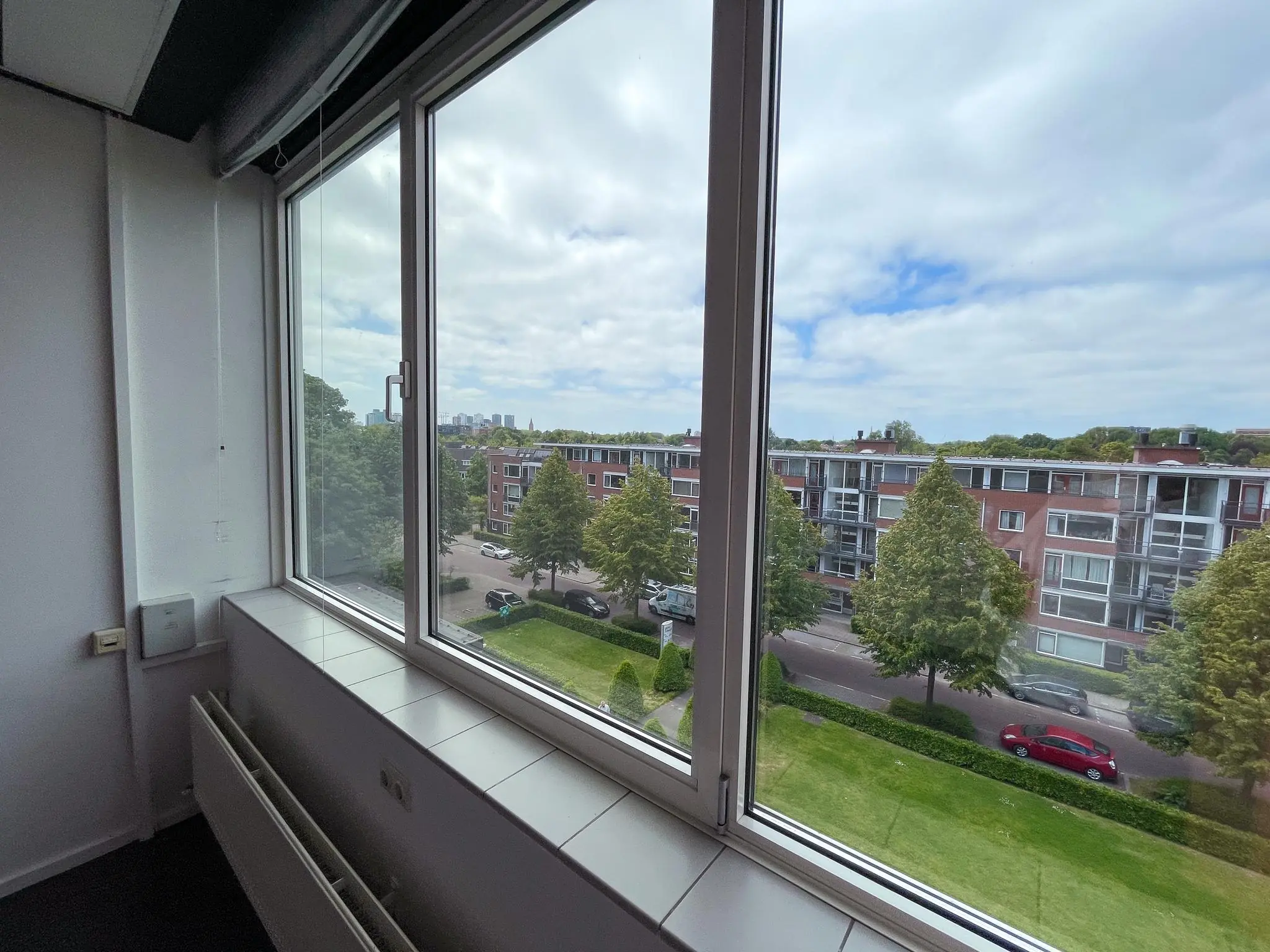 Uitzicht vanuit een hooggelegen raam op de Hengeveldstraat met appartementen, bomen en geparkeerde auto's.