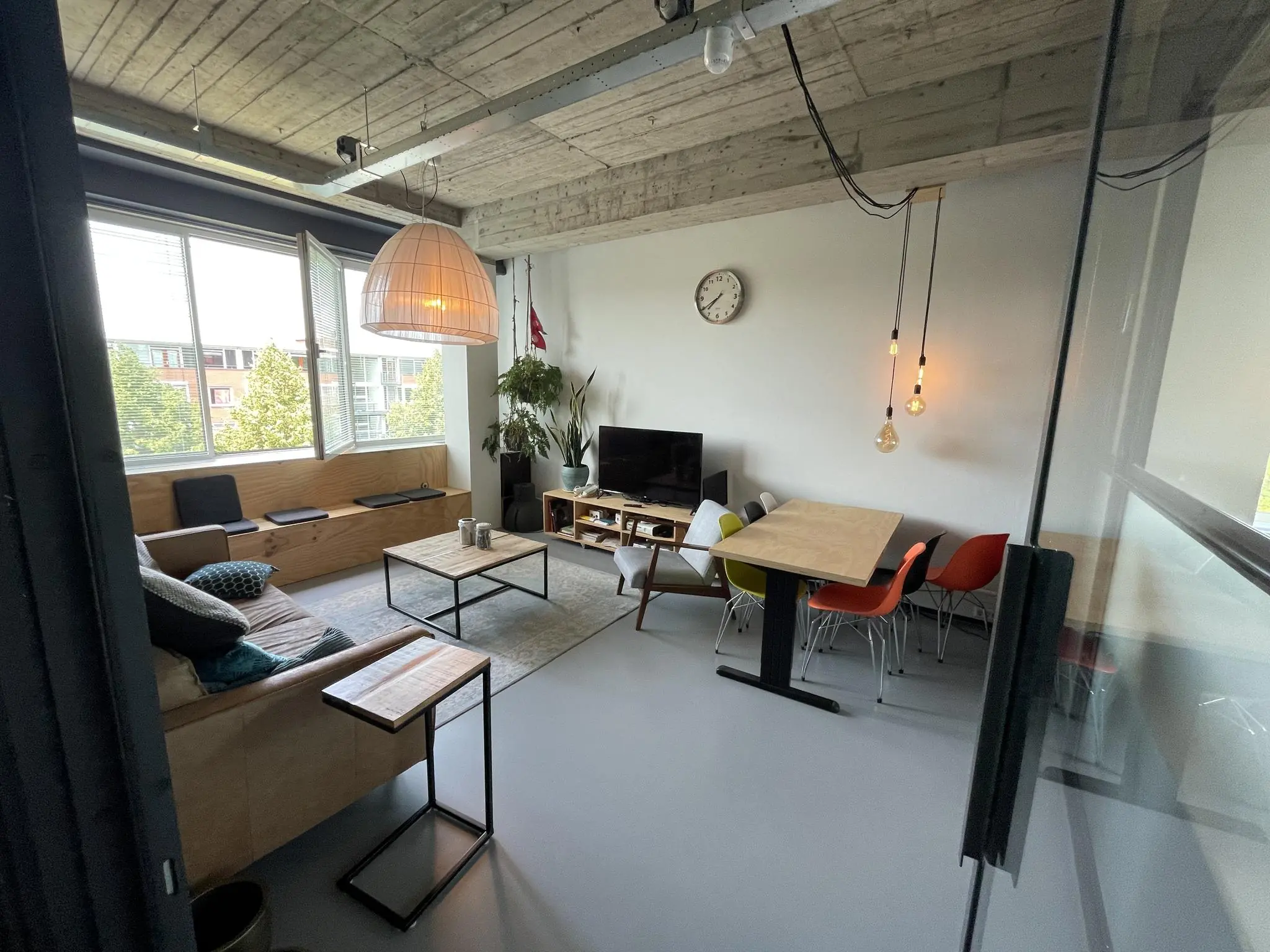 Modern ingerichte woonkamer aan de Hengeveldstraat met houten plafond, grote ramen, zithoek, eettafel en televisie.