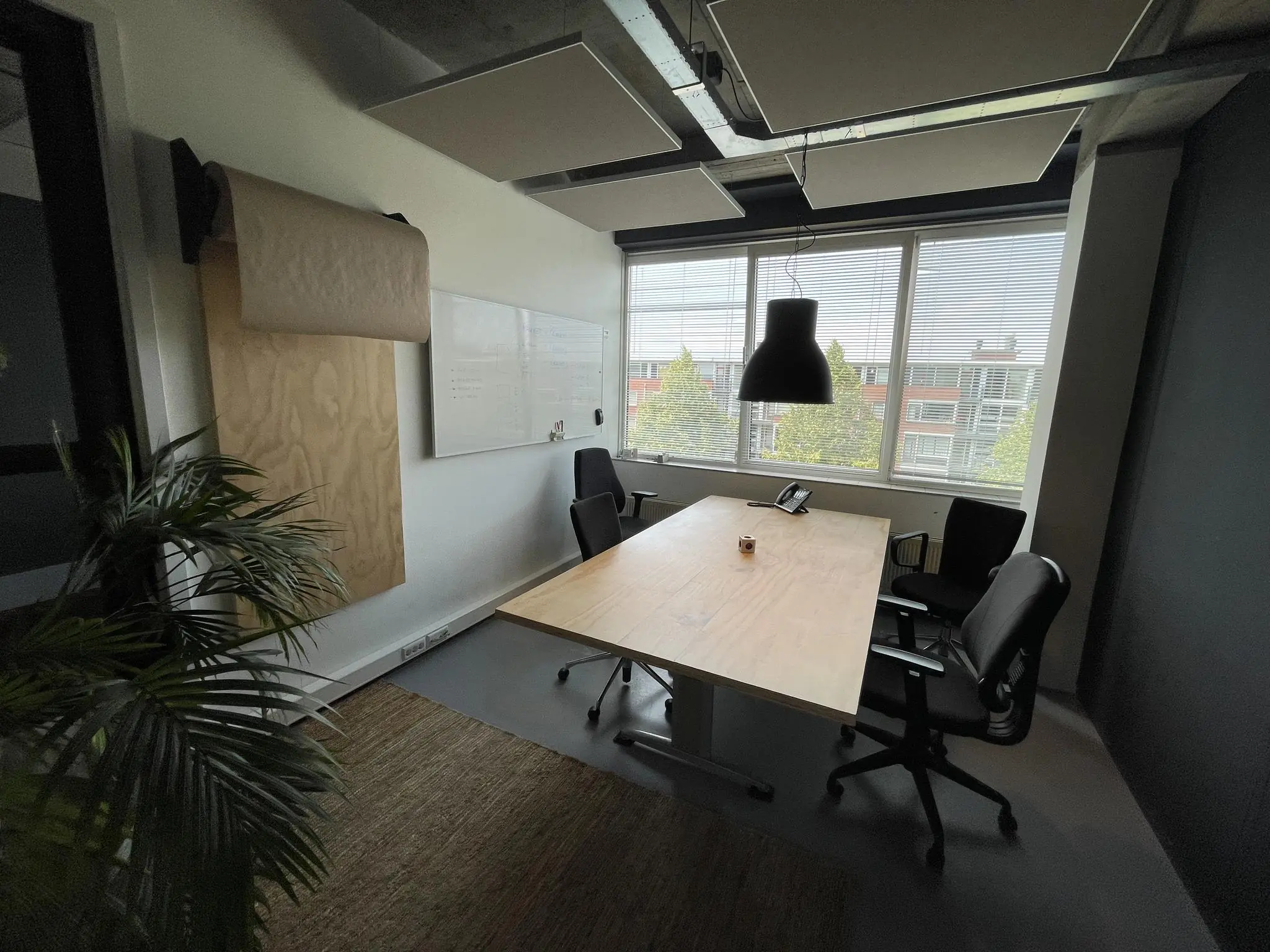 Vergaderruimte aan de Hengeveldstraat met houten tafel, vier stoelen, whiteboard en groot raam met uitzicht op een kantoorgebouw.
