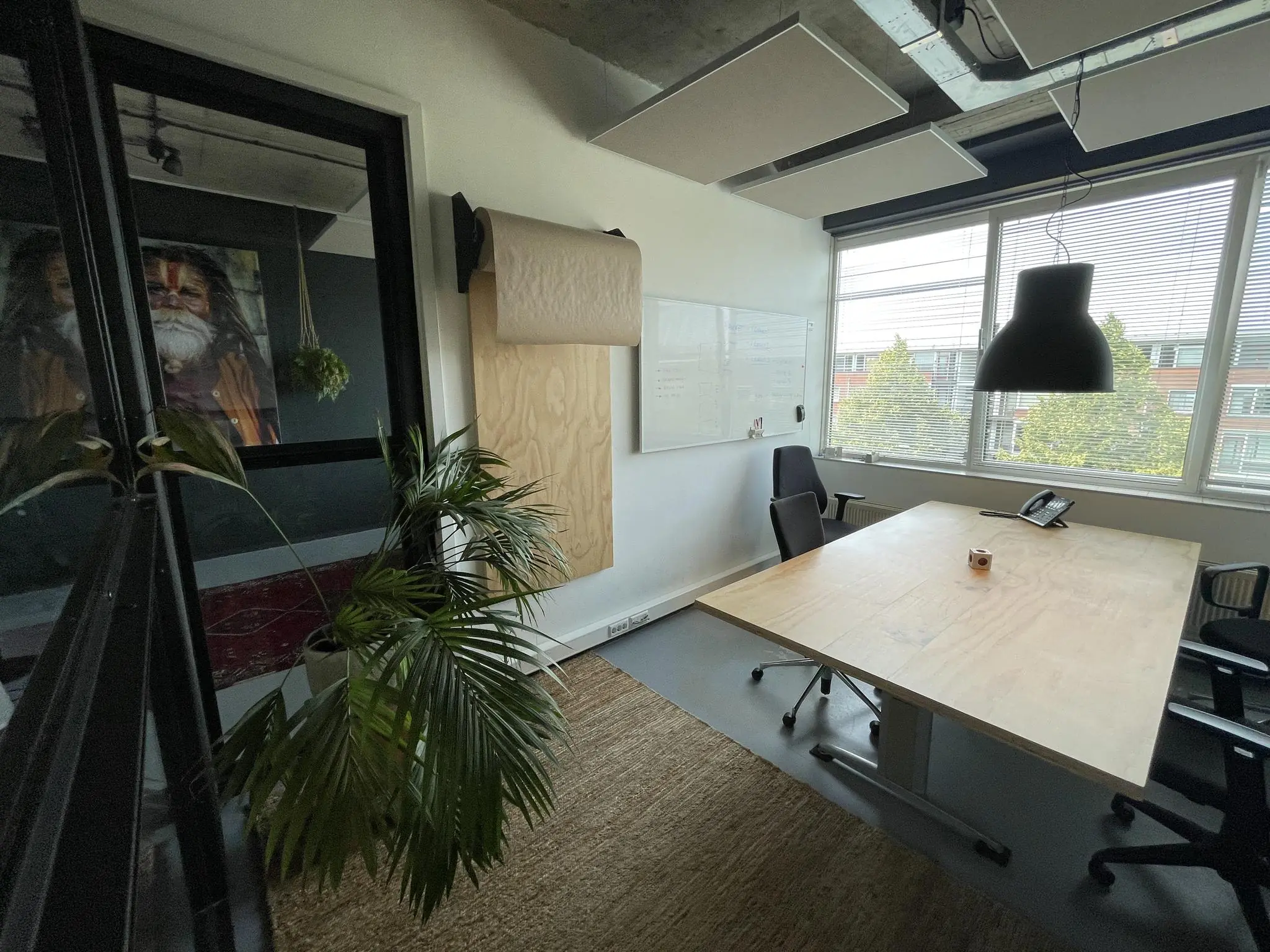 Moderne vergaderruimte aan de Hengeveldstraat met groot houten bureau, whiteboard, planten en veel daglicht.