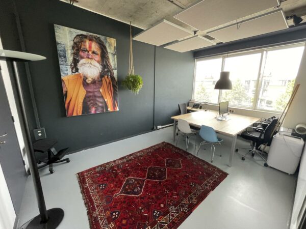 Modern kantoor aan de Hengeveldstraat met een groot bureaublad, kleurrijk tapijt en een opvallend portret aan de muur.