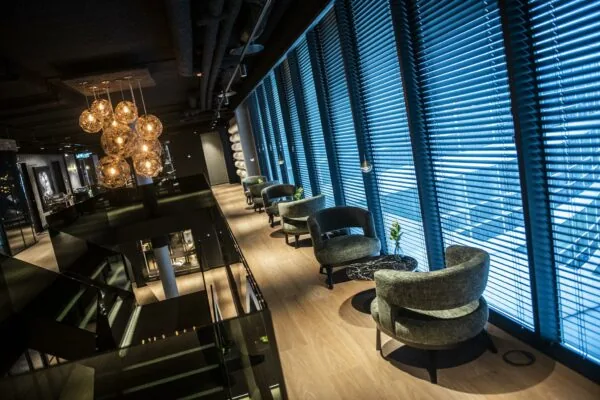 Moderne lounge in Stationspark met designstoelen, sfeerverlichting en grote ramen met jaloezieën.