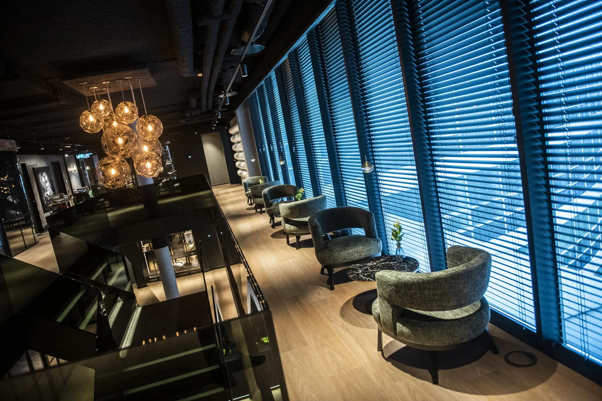 Moderne lounge in Stationspark met designstoelen, sfeerverlichting en grote ramen met jaloezieën.