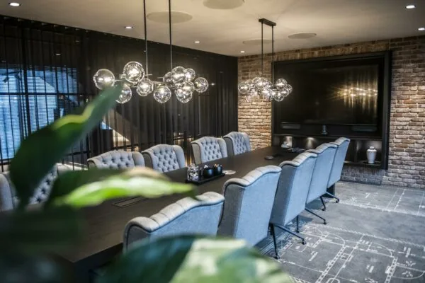 Moderne vergaderruimte in Stationspark met lange tafel, comfortabele stoelen, glazen hanglampen en bakstenen muren.