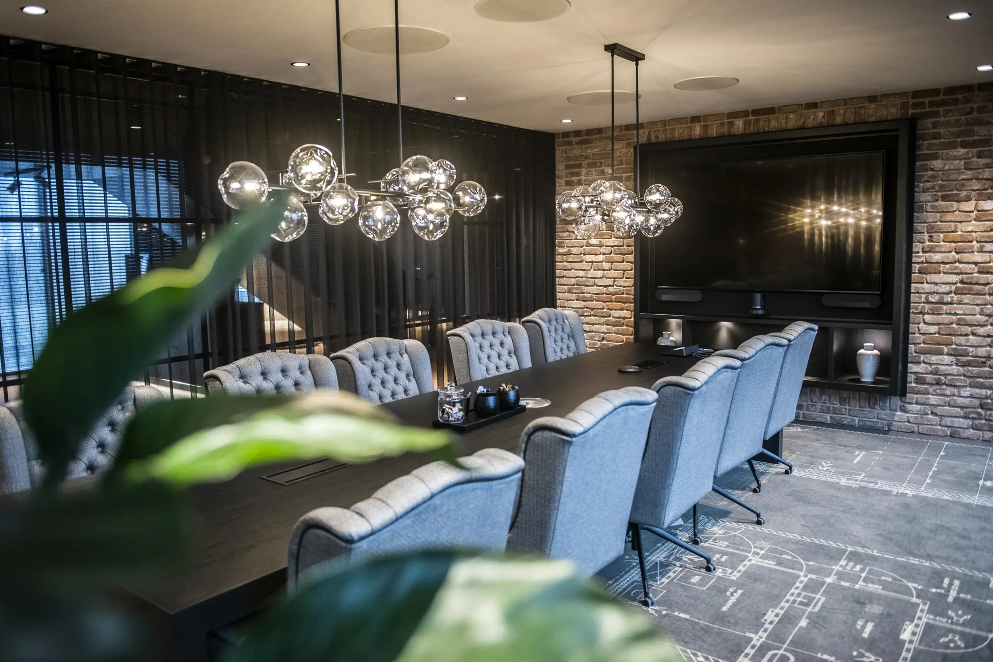 Moderne vergaderruimte in Stationspark met lange tafel, comfortabele stoelen, glazen hanglampen en bakstenen muren.