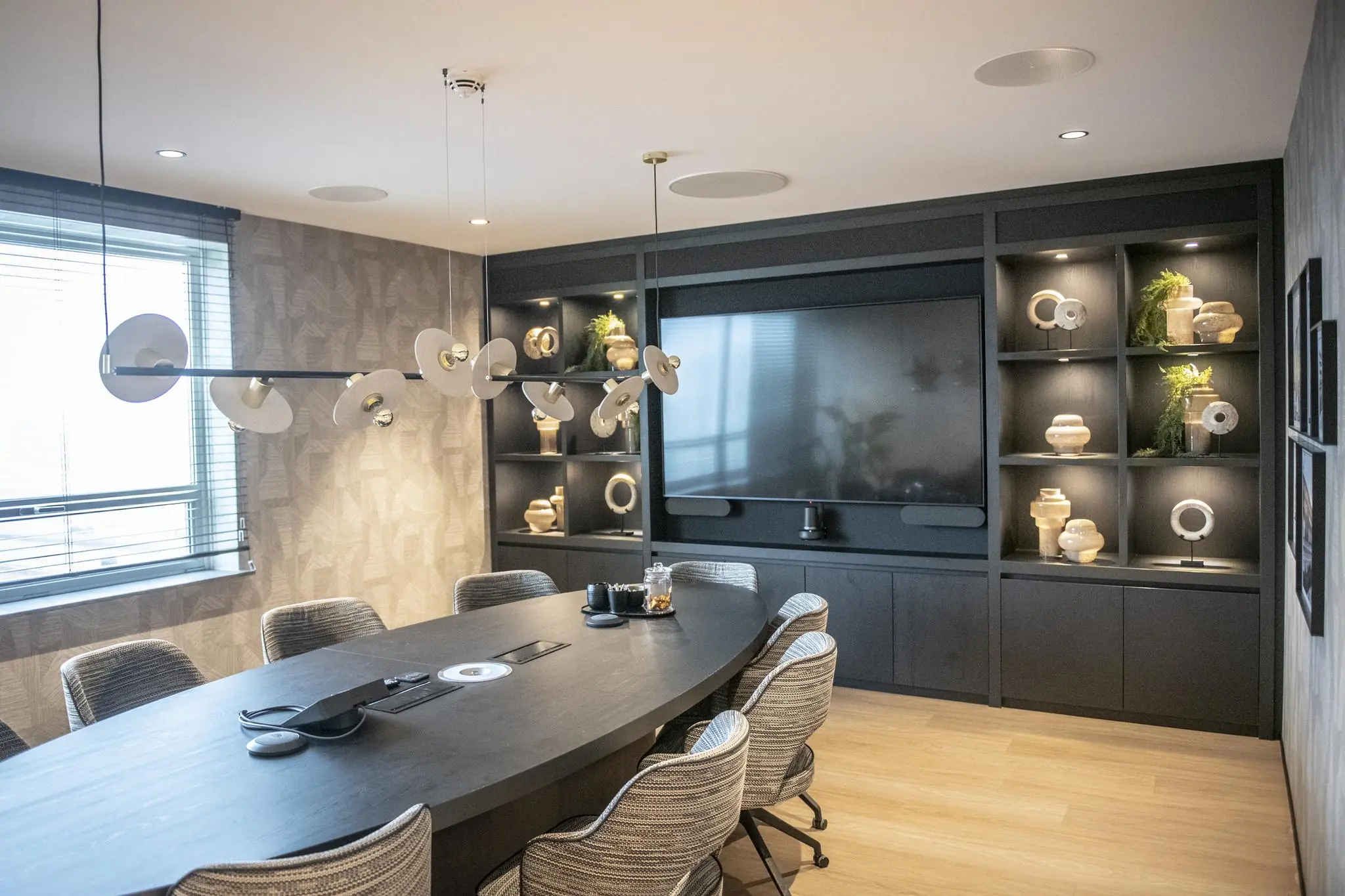 Moderne vergaderruimte in Stationspark met een ovale tafel, designverlichting, ingebouwde kast met decoratieve objecten en een groot beeldscherm.