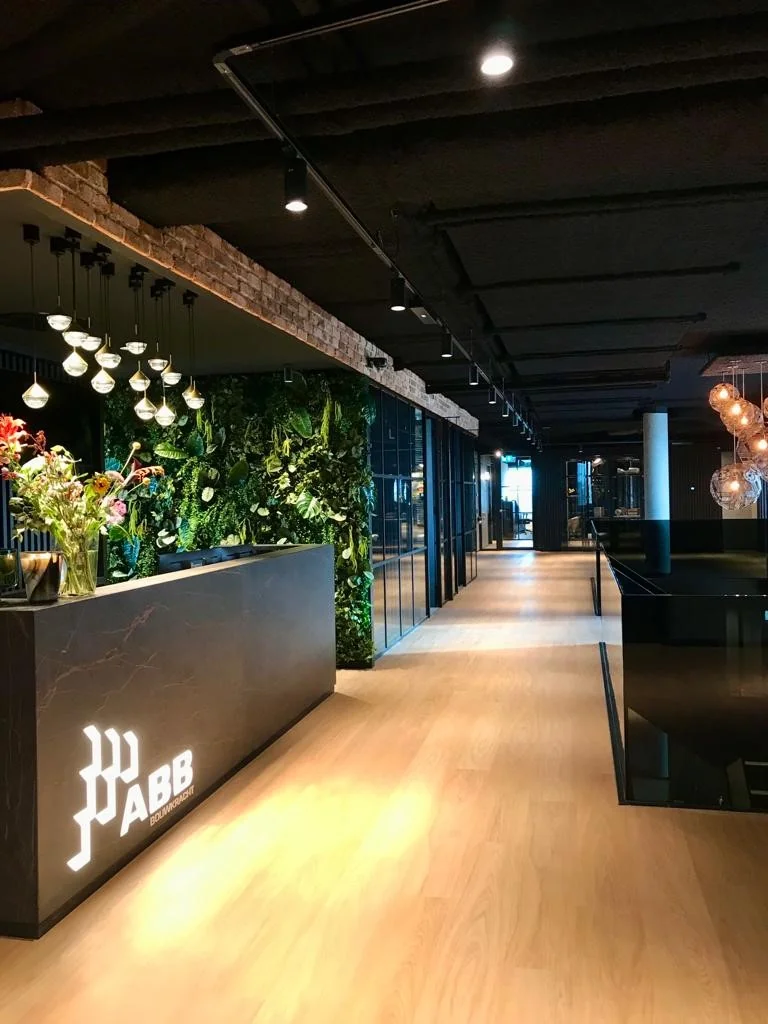Moderne kantoorruimte van ABB Bouwnadvies met houten vloer, groene plantenwand en stijlvol verlichte receptiebalie.