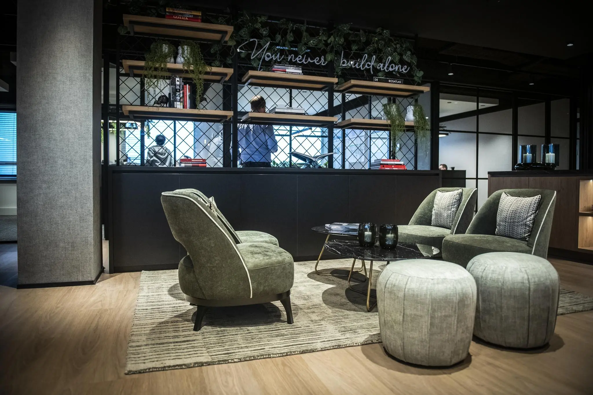 Moderne loungehoek in Stationspark met groene fauteuils, ronde poefs en een zwarte salontafel op een licht vloerkleed.