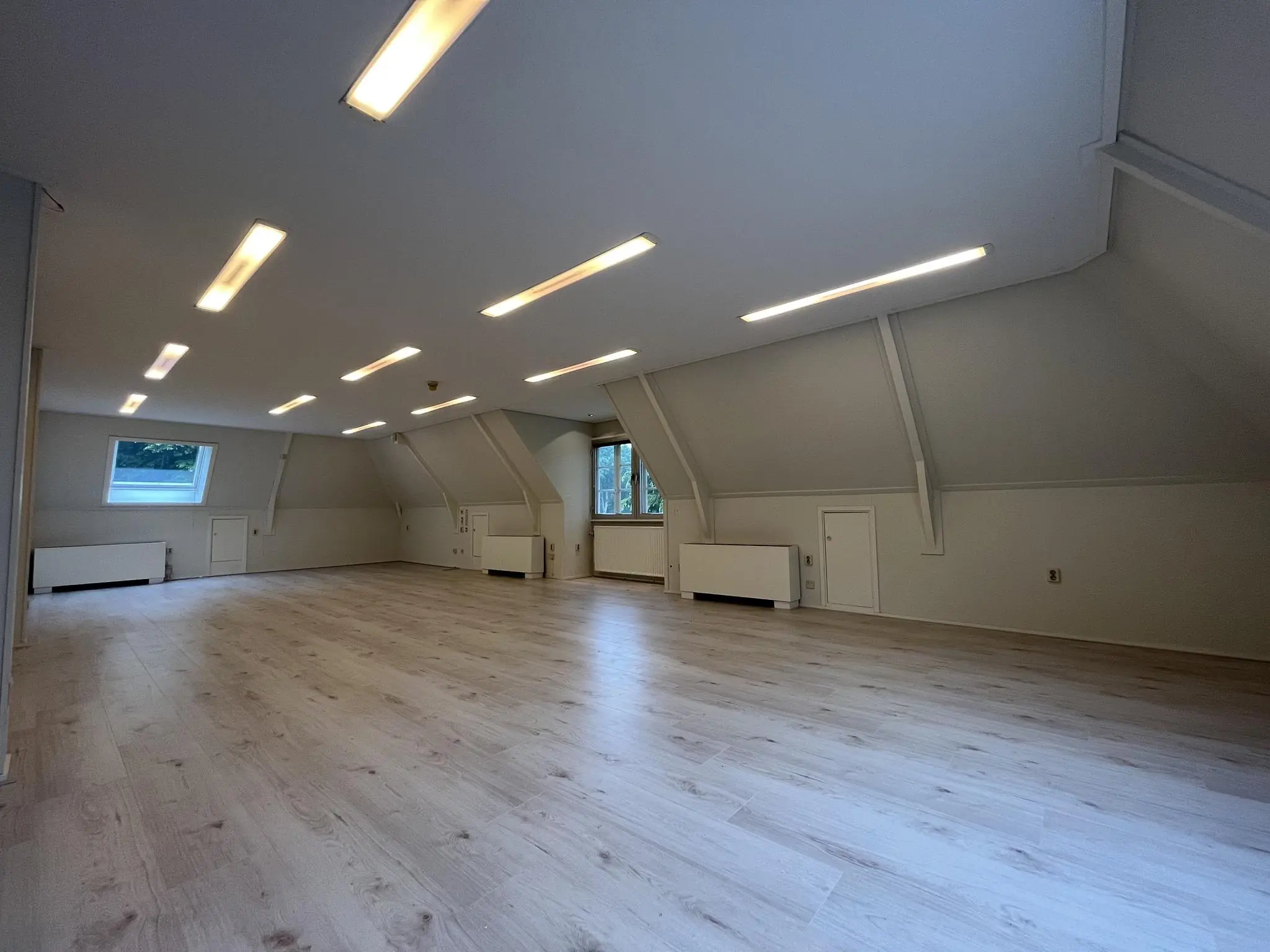 Ruime, lege zolderkamer met schuin dak, lichte houten vloer en ingebouwde verlichting aan de Amersfoortsestraat.