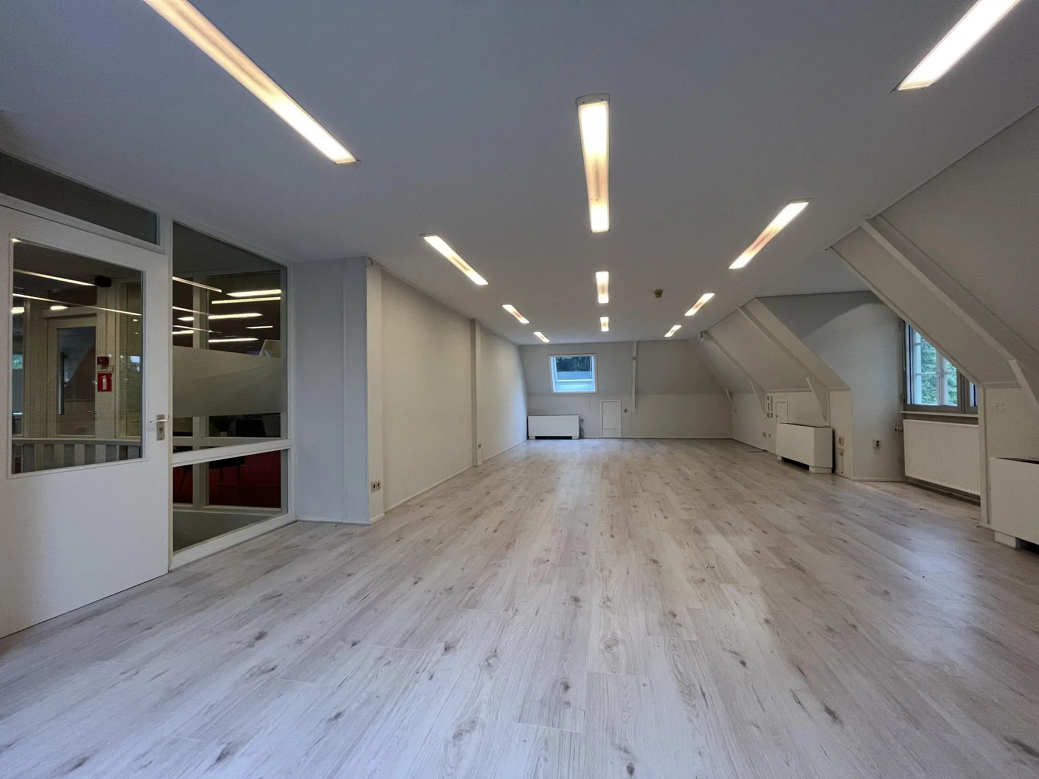 Lege kantoorruimte aan de Amersfoortsestraat met licht laminaat, witte muren en ingebouwde plafondverlichting.