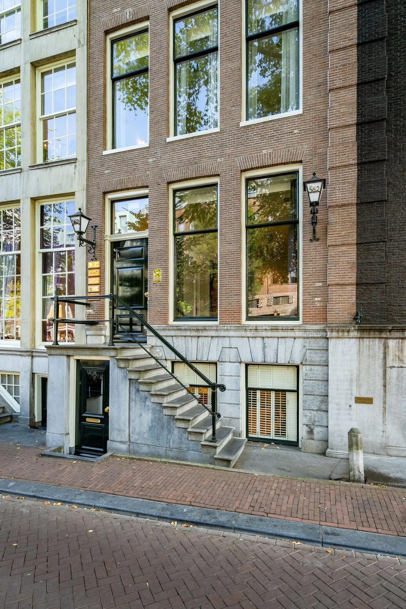 Gevel van een klassiek Amsterdams grachtenpand aan de Herengracht met hoge ramen en een stoeptrap.