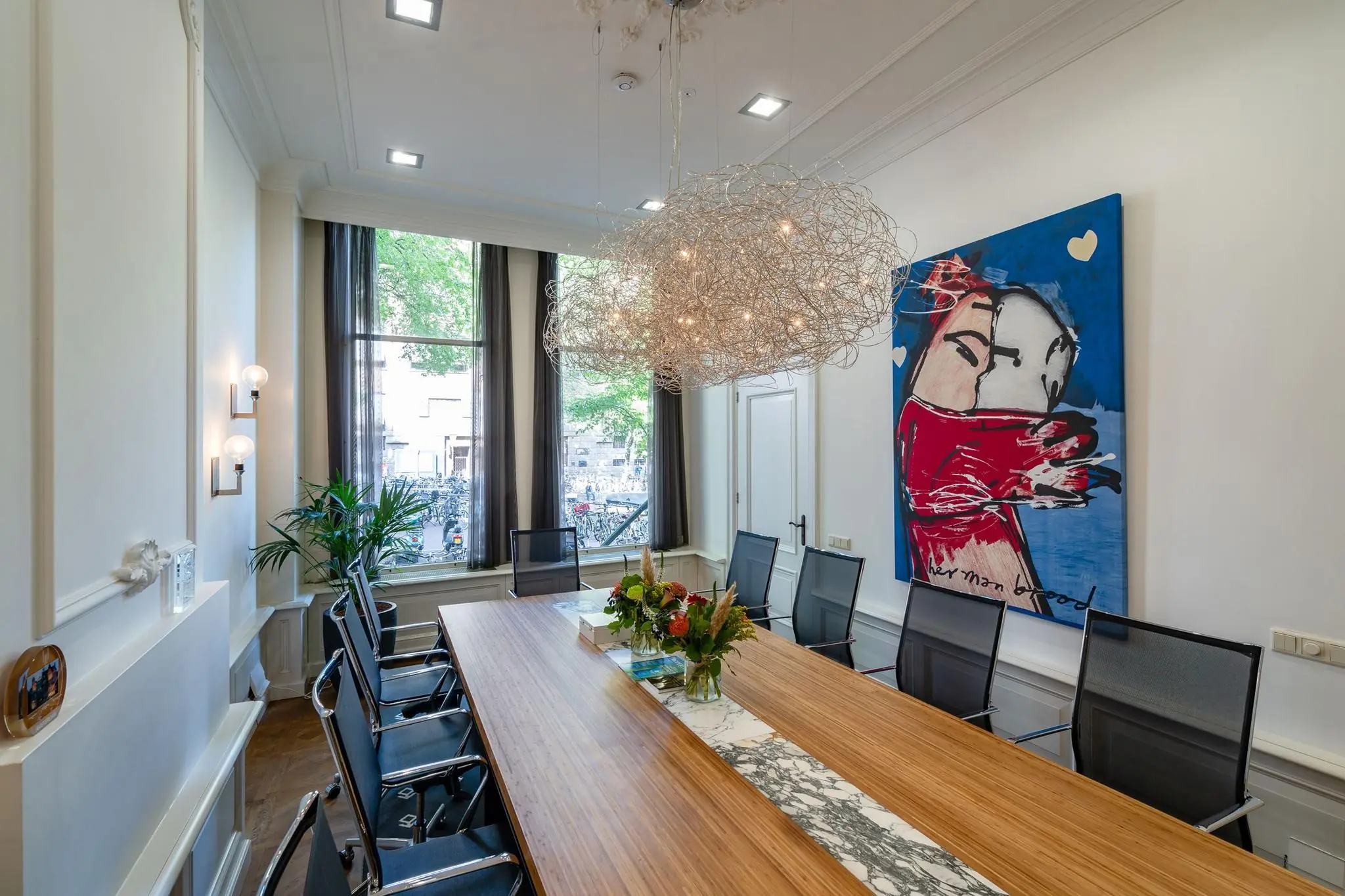 Vergaderruimte aan de Herengracht met modern kunstwerk van Herman Brood en designverlichting boven een houten tafel.