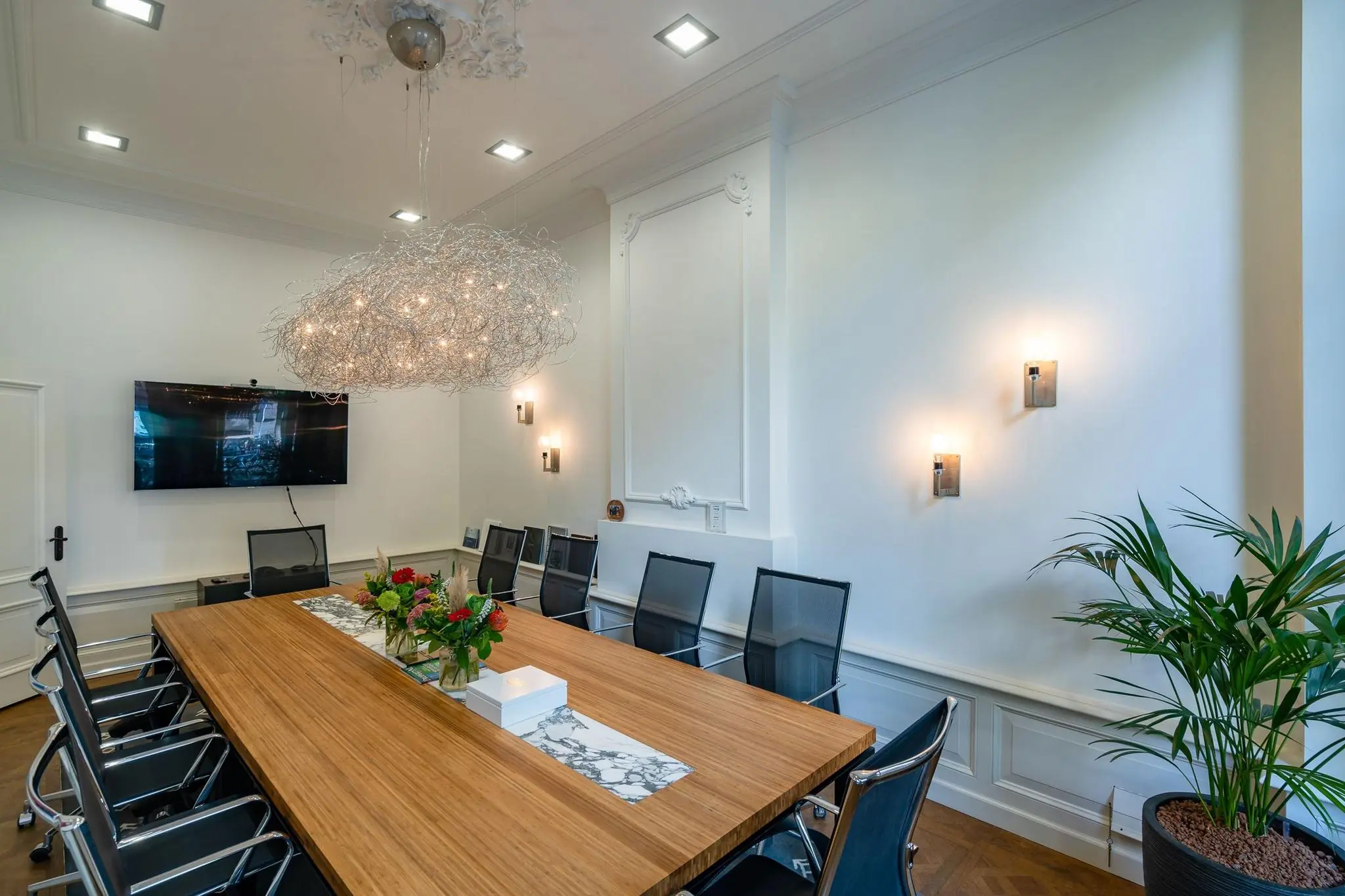 Vergaderruimte aan de Herengracht met houten tafel, moderne stoelen, sierlijke plafondlamp en wandverlichting.