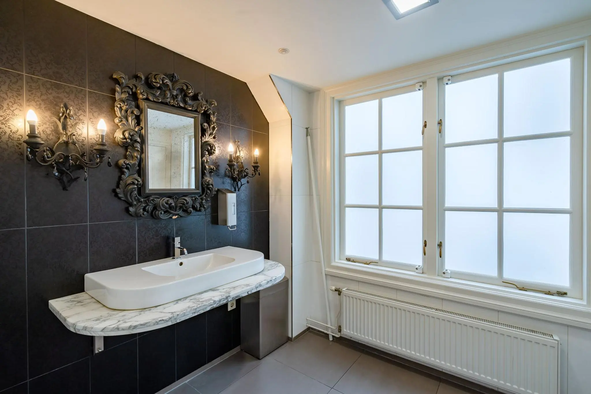 Luxe badkamer aan de Herengracht met marmeren wastafel, sierlijke spiegel en wandarmaturen in barokstijl.