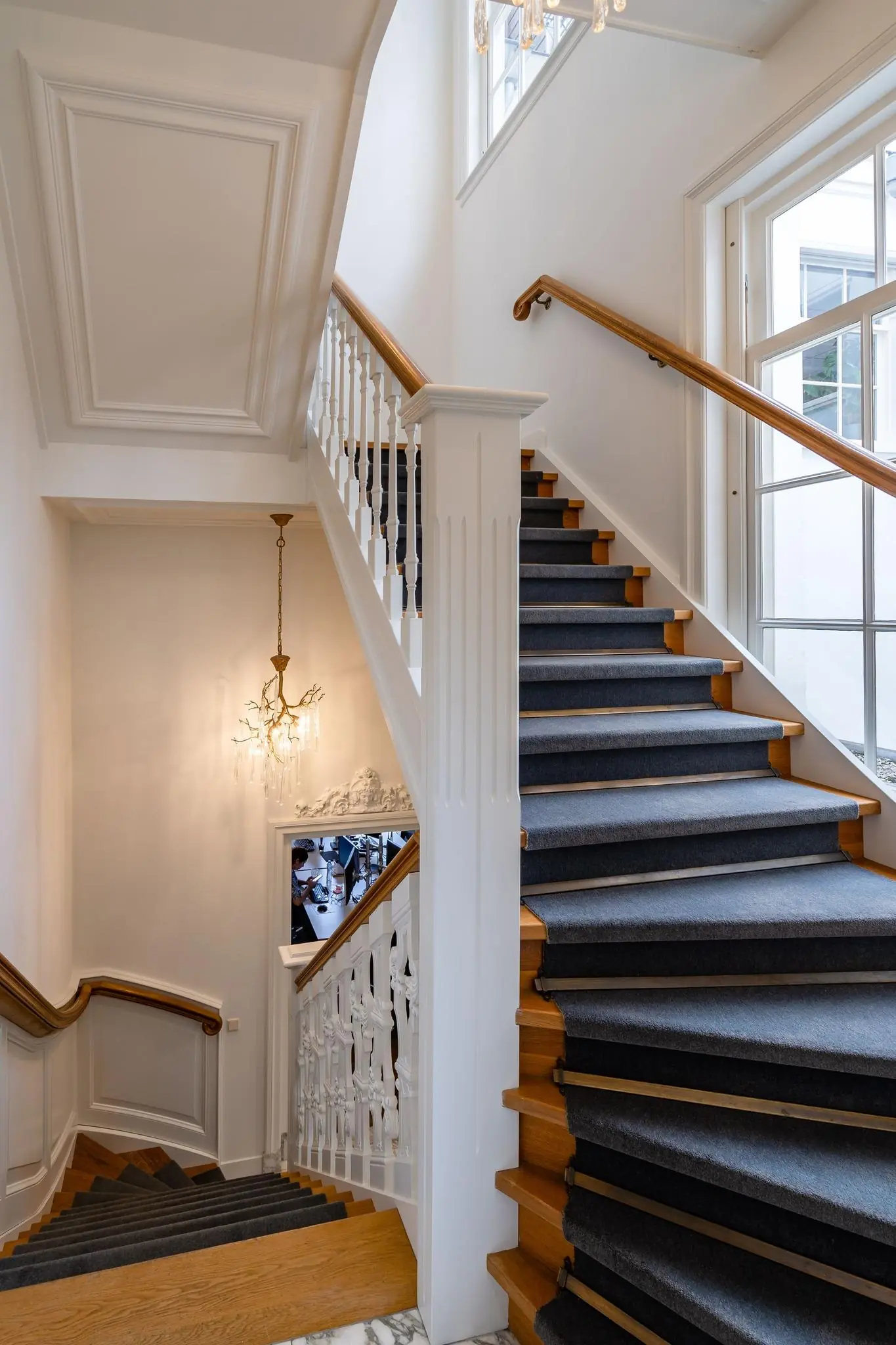 Trap met houten treden en donker tapijt in een klassiek herenhuis aan de Herengracht, met een sierlijke balustrade en kroonluchter.