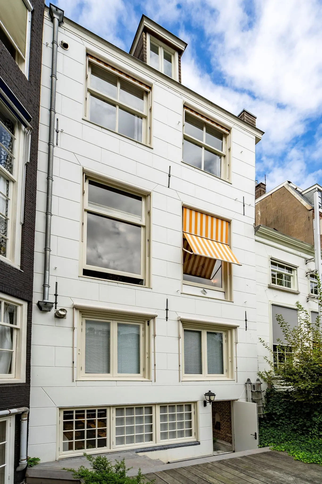 Witgevel pand aan de Herengracht met grote ramen en een geel-wit gestreept zonnescherm.