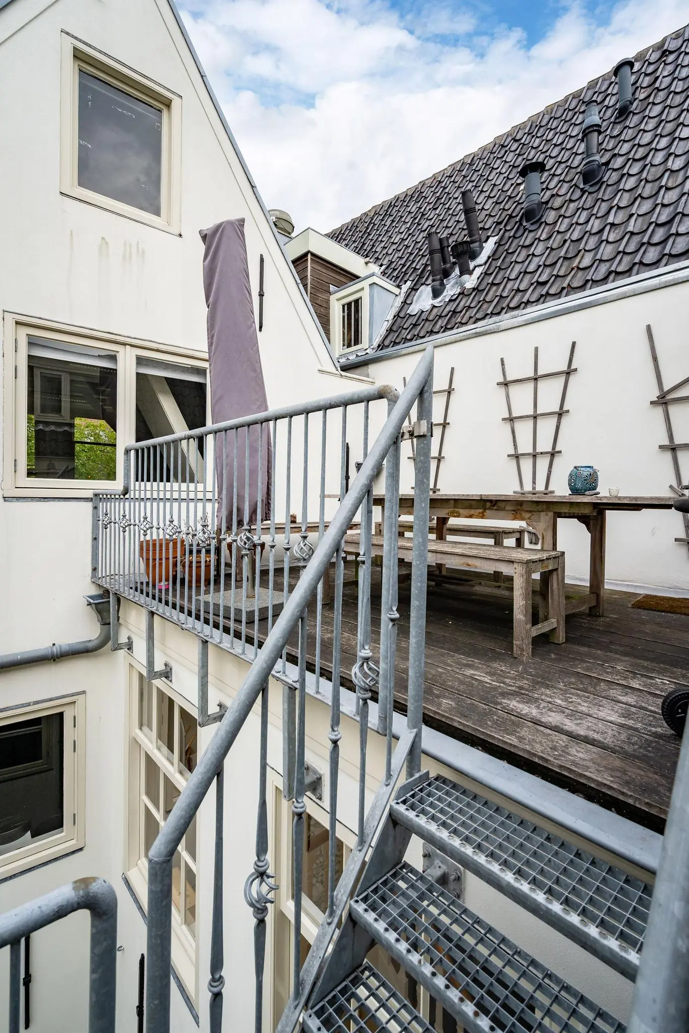 Buiten terras aan de Herengracht met houten tuinmeubilair en metalen trap naar beneden.