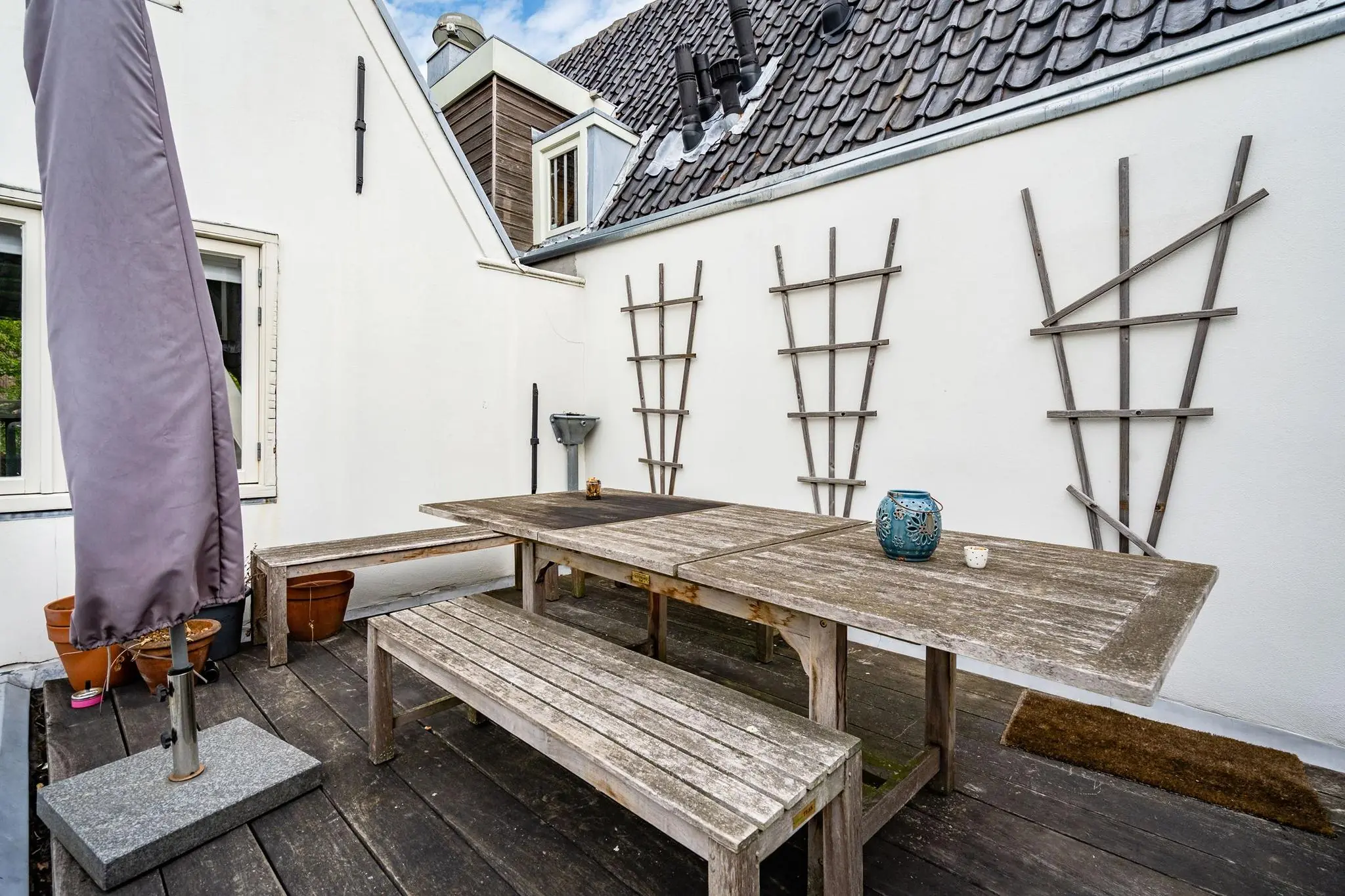 Houten dakterras aan de Herengracht met picknicktafel, banken en een opgevouwen parasol.