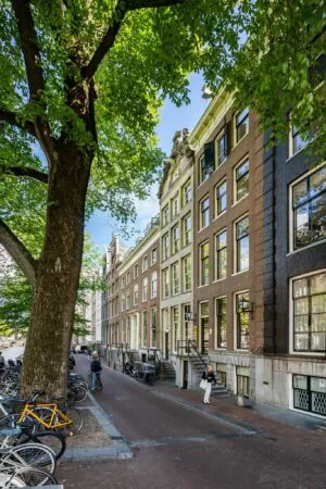 Gevels van klassieke grachtenpanden aan de Herengracht in Amsterdam, met een boomrijke straat en geparkeerde fietsen.