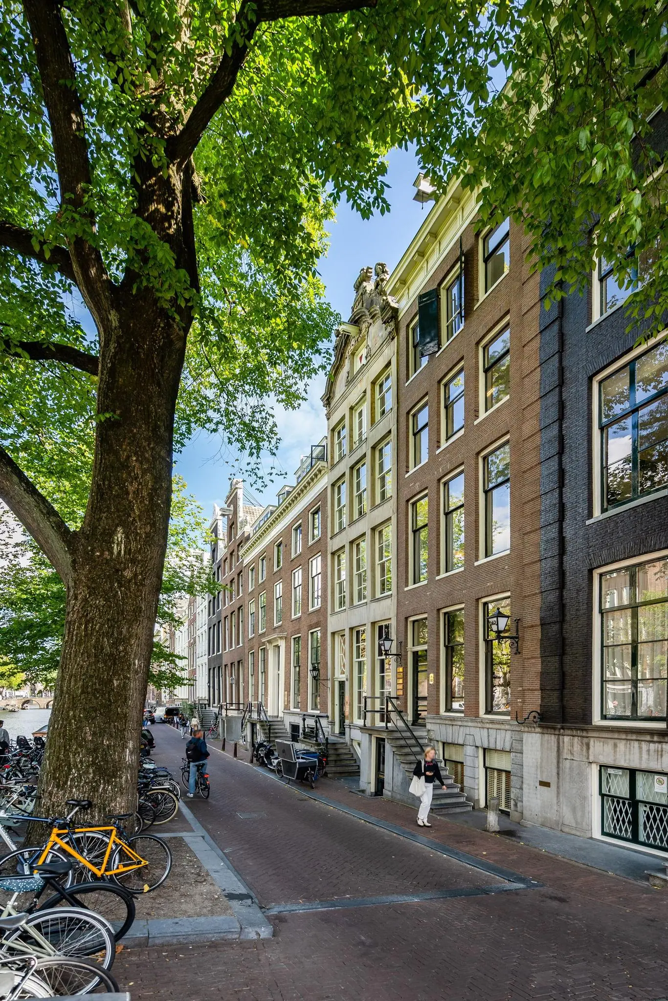 Gevels van klassieke grachtenpanden aan de Herengracht in Amsterdam, met een boomrijke straat en geparkeerde fietsen.
