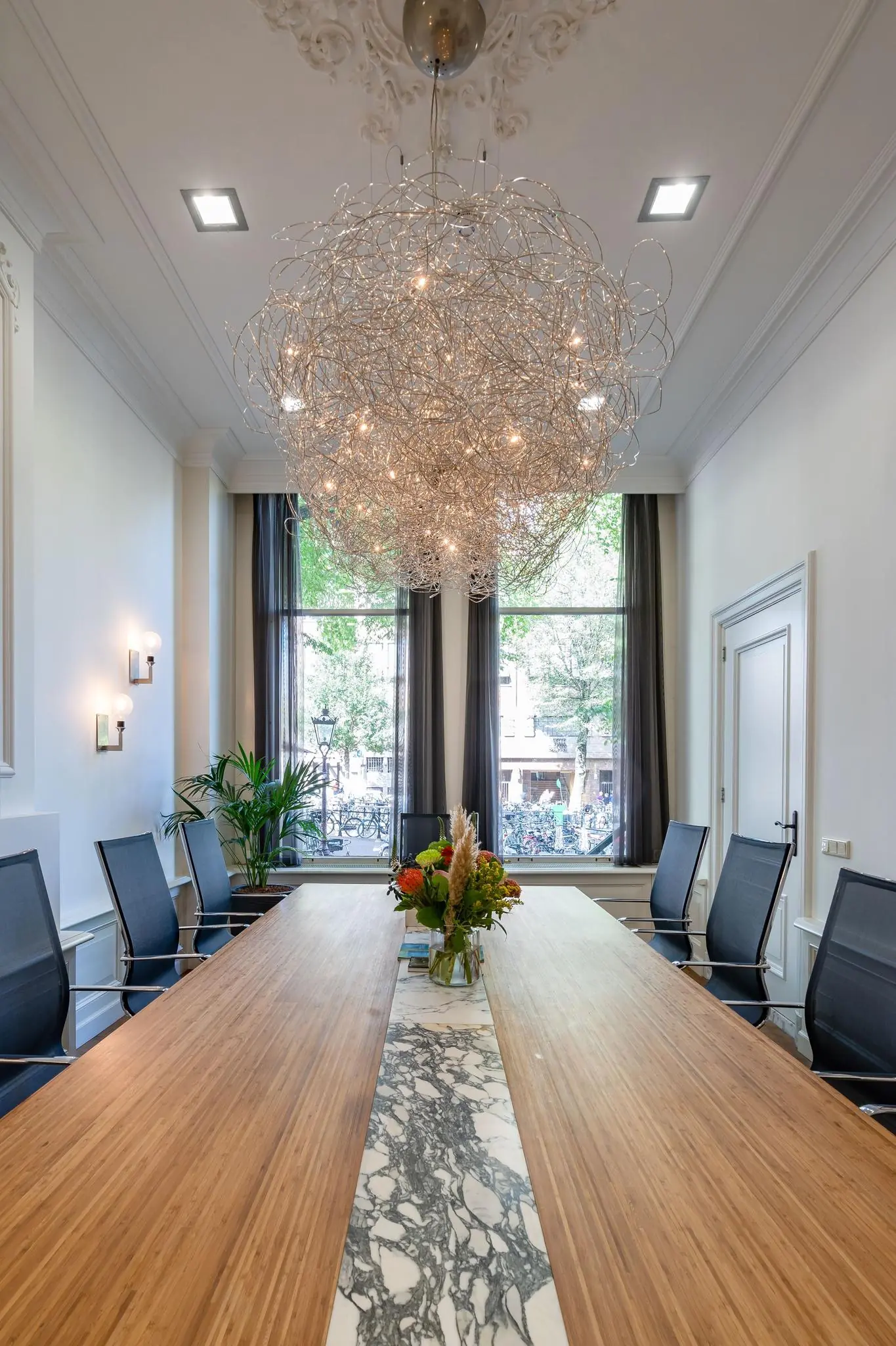 Vergaderruimte aan de Herengracht met een lange houten tafel, moderne stoelen, grote ramen en een opvallende designlamp.
