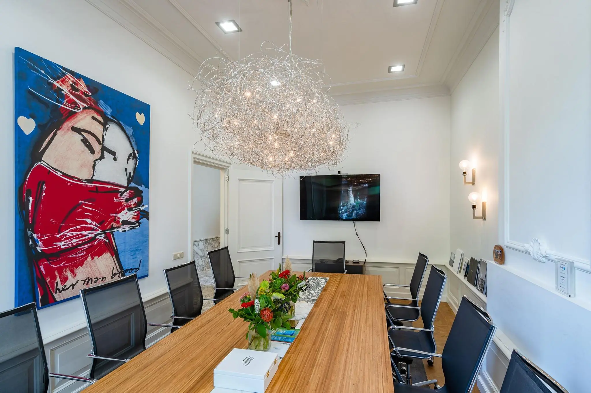 Vergaderruimte aan de Herengracht met een lange houten tafel, moderne stoelen, opvallende hanglamp, kunstwerk van een omhelzing en een flatscreen aan de muur.