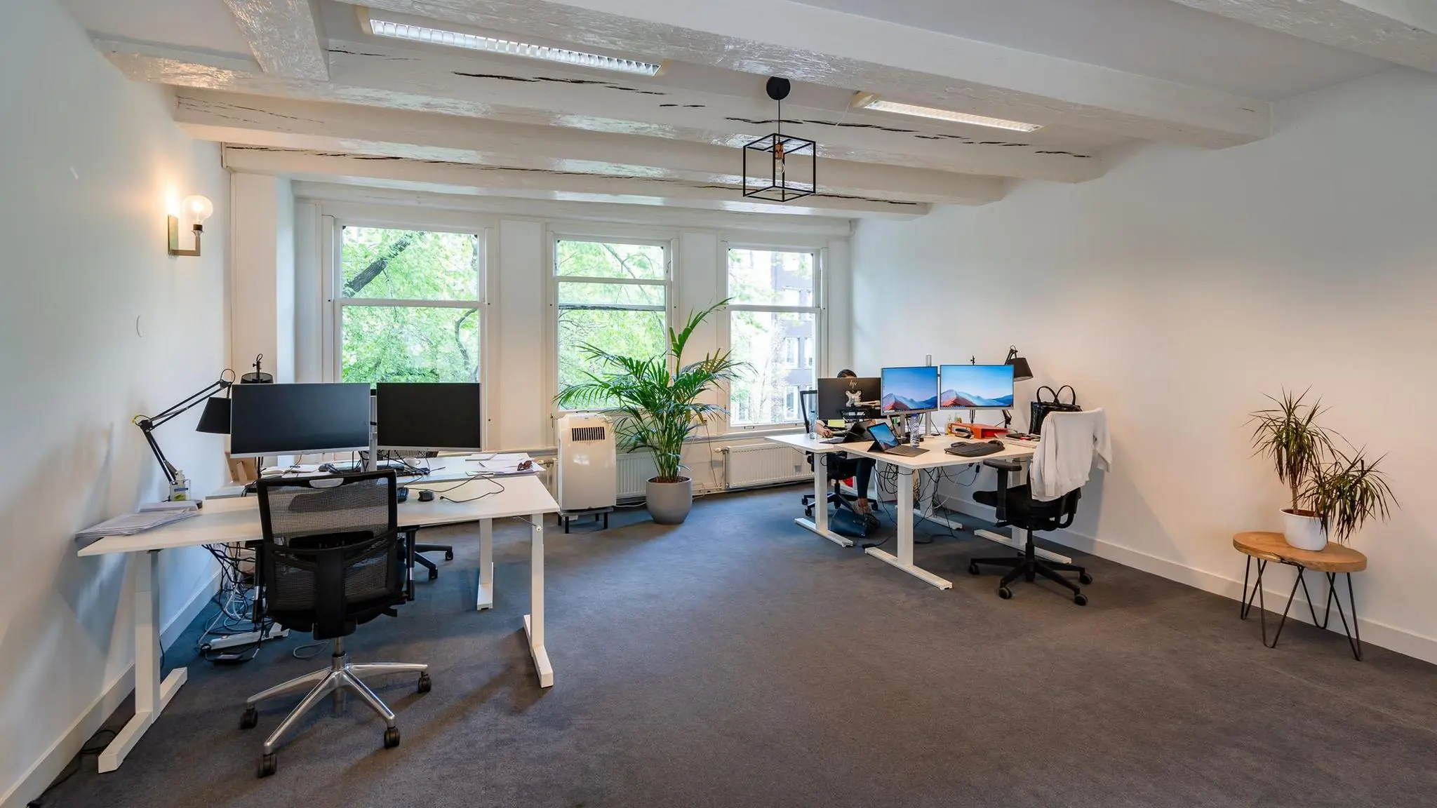 Modern kantoorinterieur aan de Herengracht met werkplekken, grote ramen en houten plafondbalken.