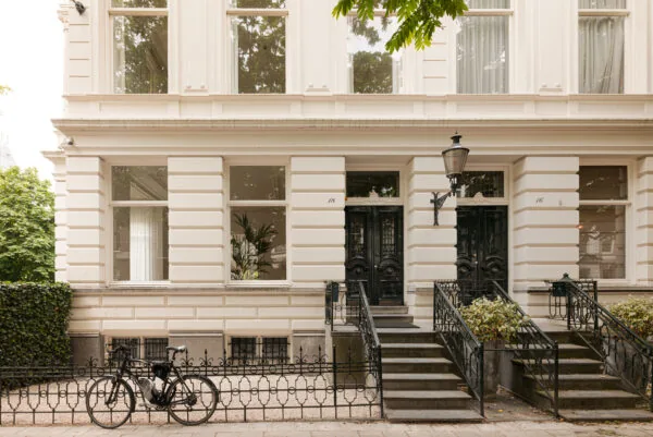 Wit herenhuis aan de Weteringschans met twee zwarte voordeuren, sierlijke trappen en een geparkeerde racefiets op de stoep.