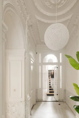 Elegante witte entreehal aan de Weteringschans met sierplafond, marmeren lambrisering en moderne hanglamp.