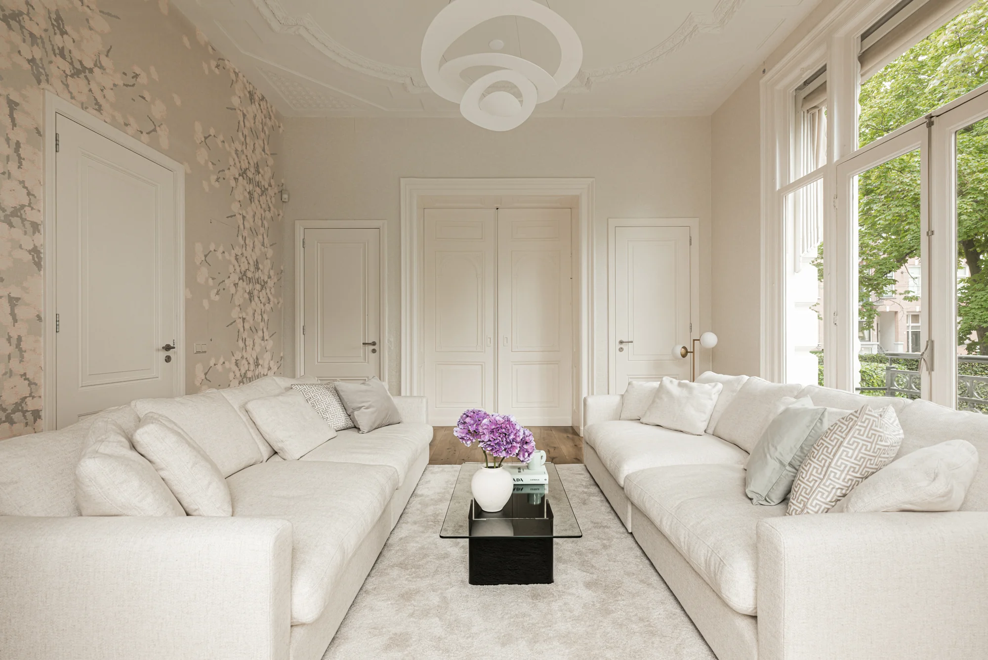 Licht en elegant ingericht woonkamerinterieur aan de Weteringschans met twee crèmekleurige banken, een glazen salontafel en grote ramen.