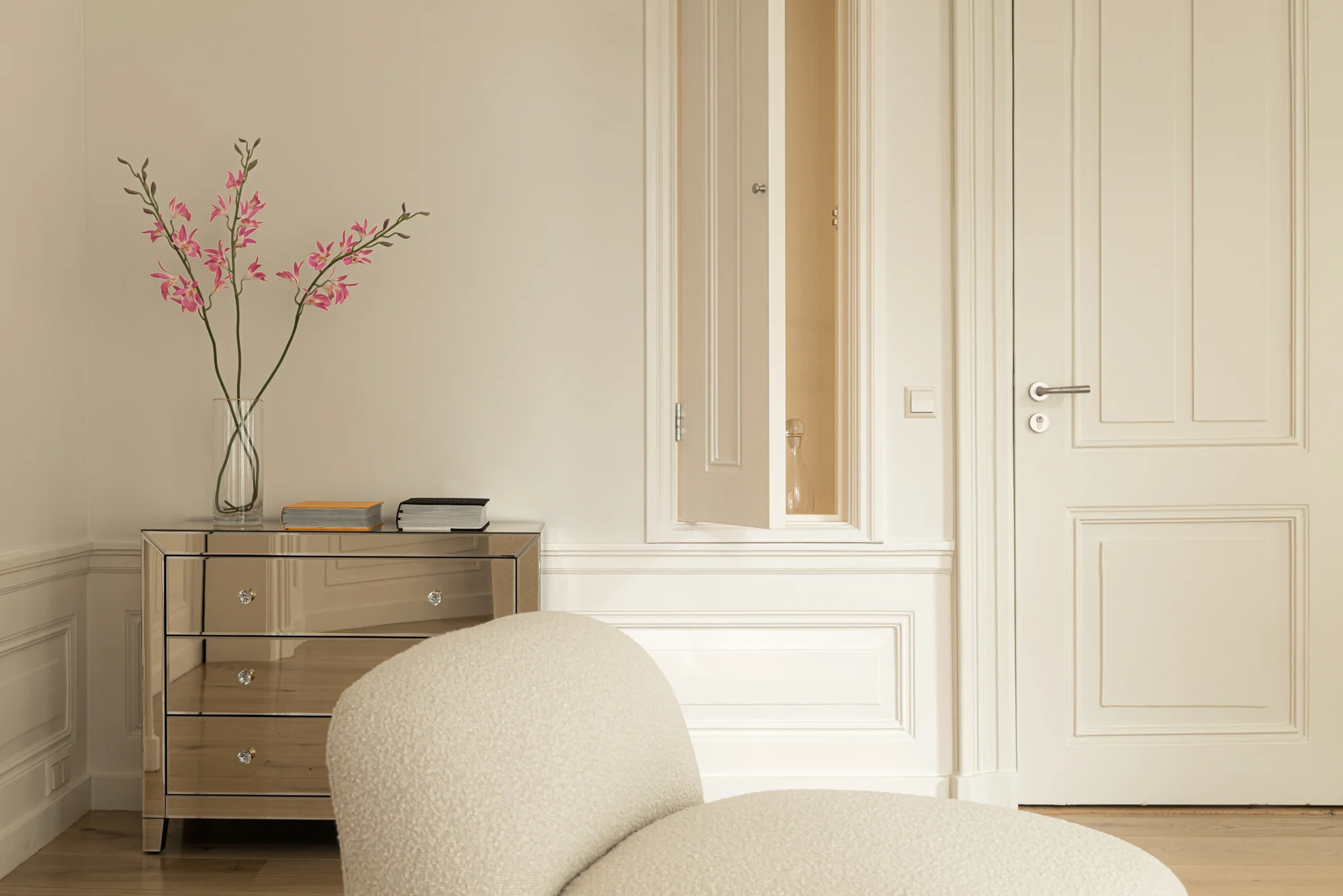 Licht interieur met een spiegelkast, roze bloemen in een vaas en een open wandkastje aan de Weteringschans.