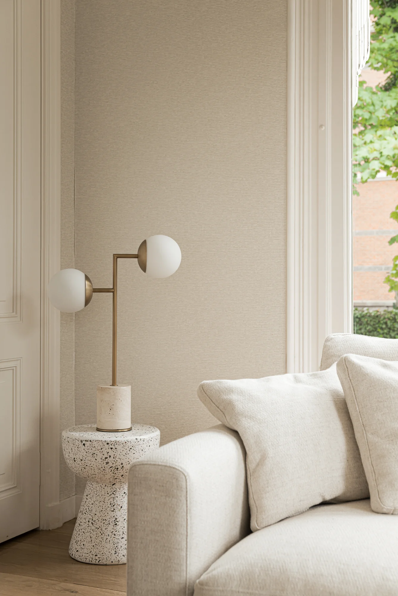 Moderne interieurhoek met een beige bank, een terrazzo bijzettafeltje en een designlamp bij een groot raam aan de Weteringschans.