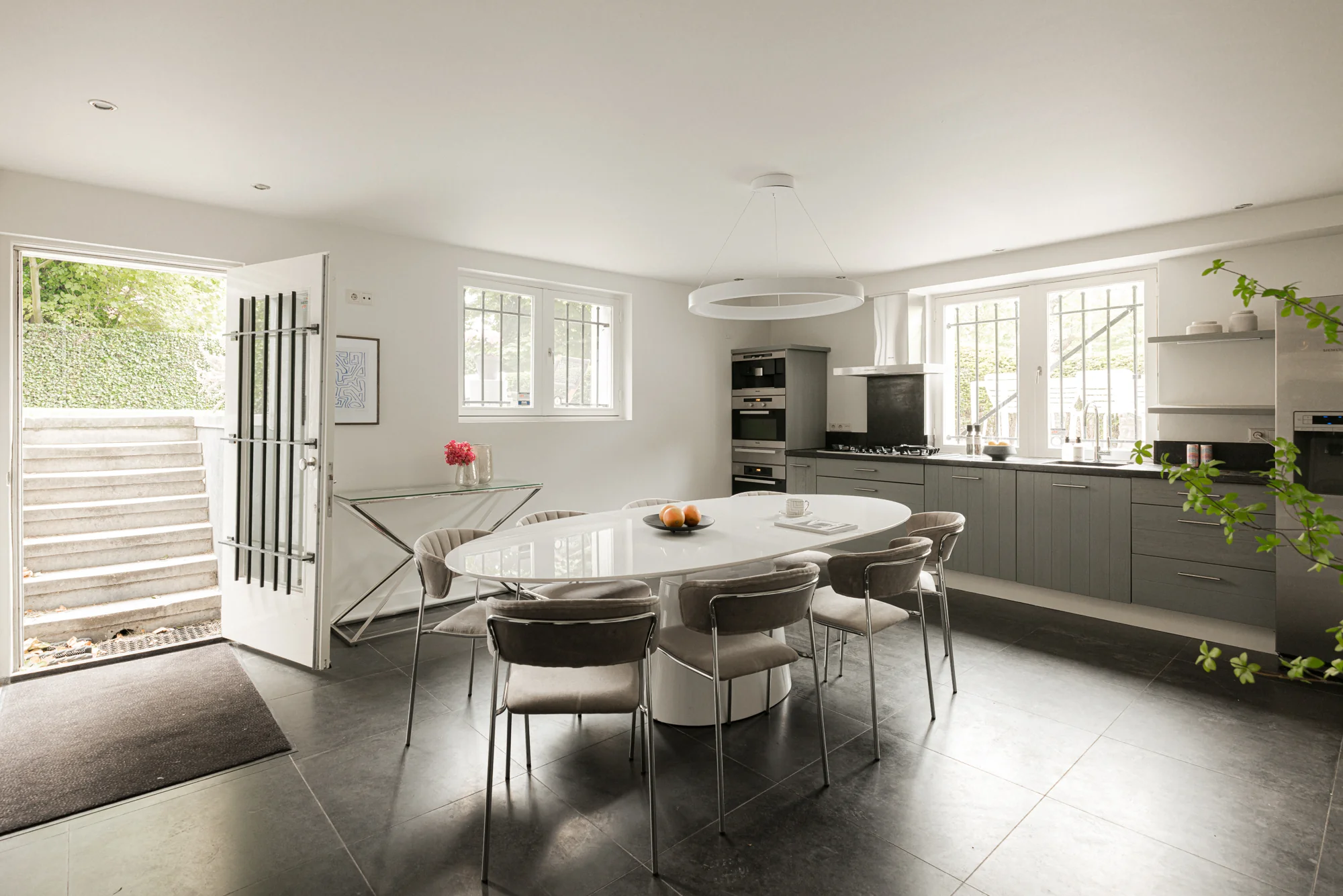 Moderne, lichte woonkeuken aan de Weteringschans met een groot ovaal wit eettafel, grijze keukenkasten en uitzicht op een buitentrap.