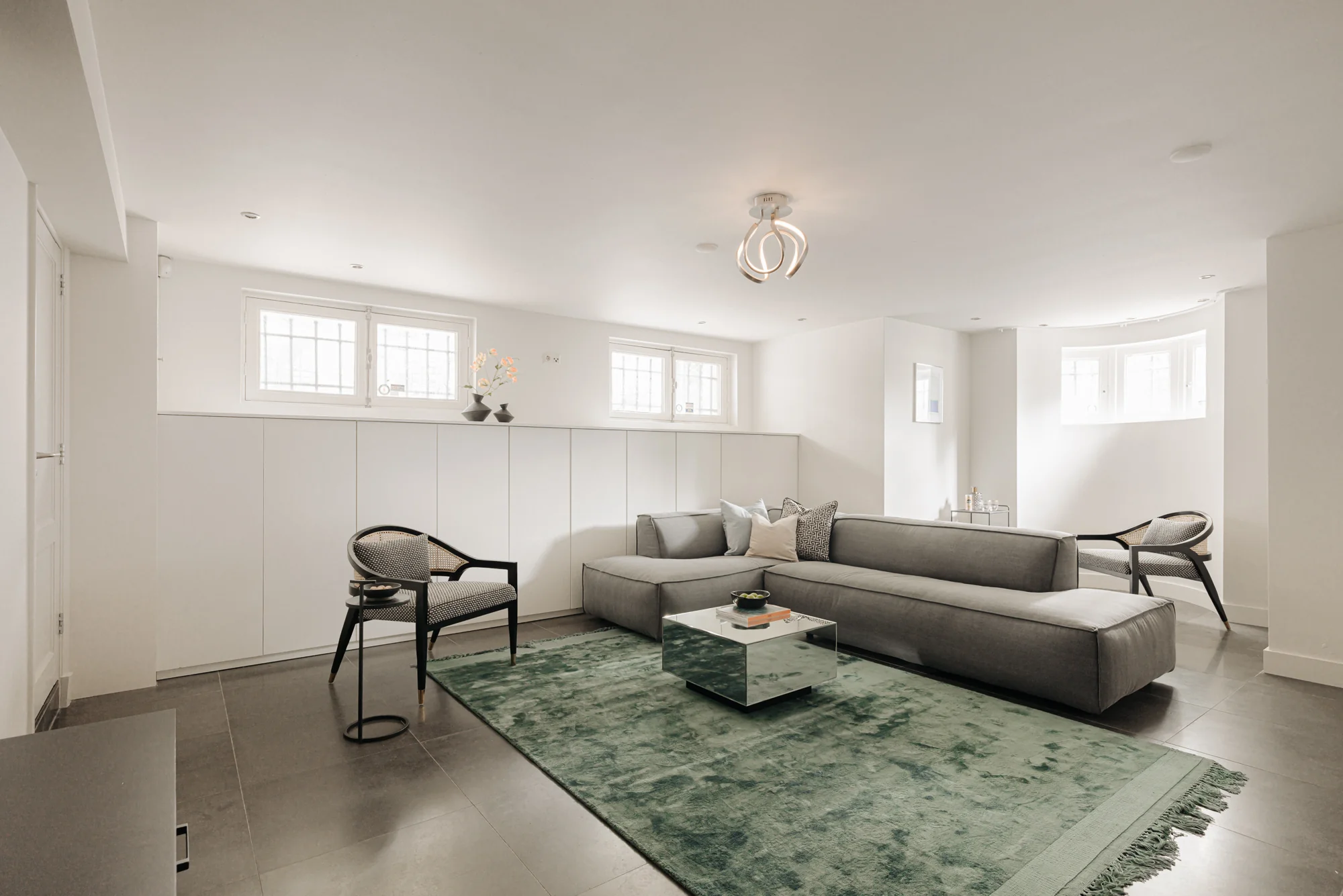Moderne, minimalistisch ingerichte woonkamer aan de Weteringschans met een grijze hoekbank, groene vloerkleed en veel natuurlijk licht.