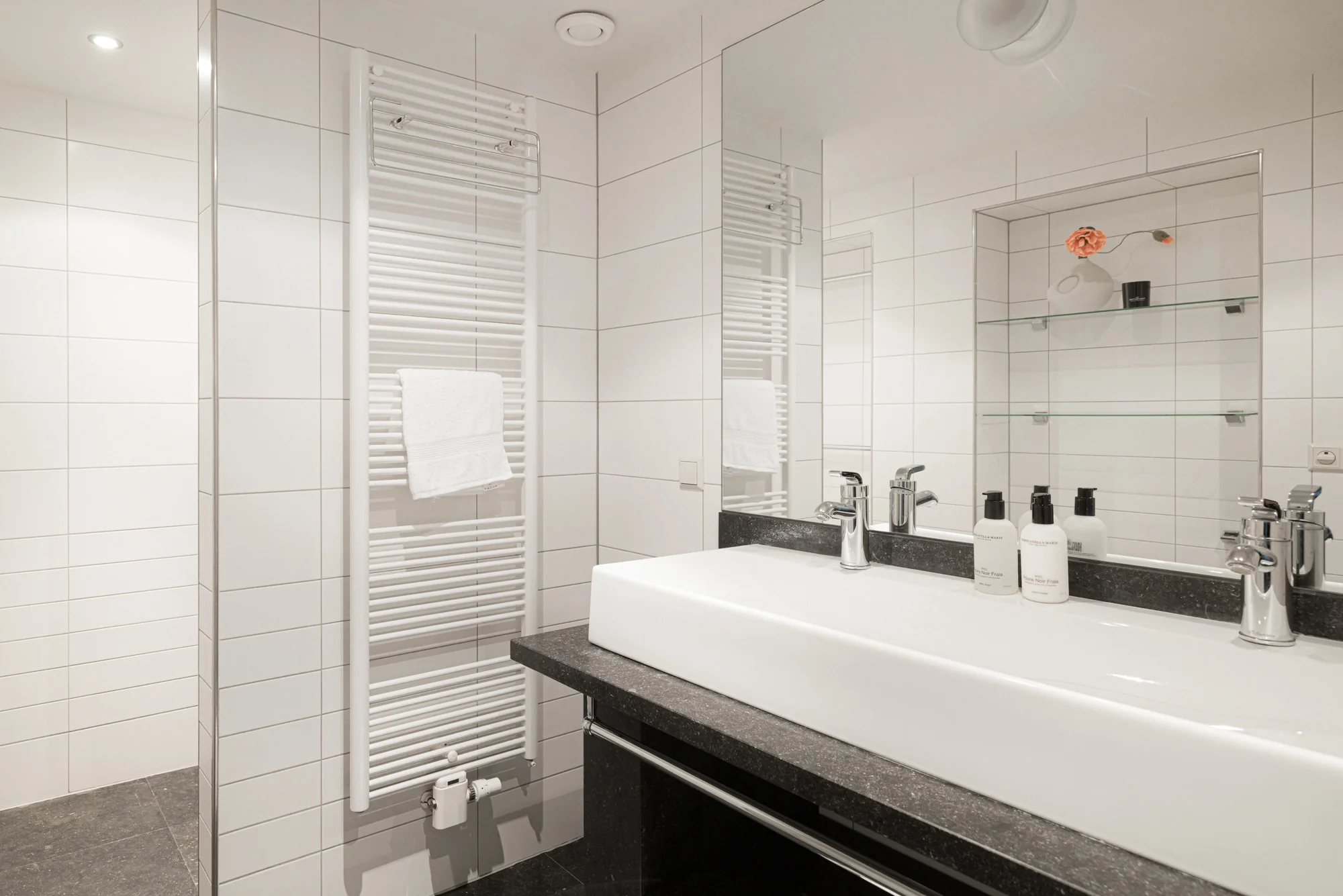 Moderne, wit betegelde badkamer aan de Weteringschans met dubbele wastafel, grote spiegel en handdoekradiator.
