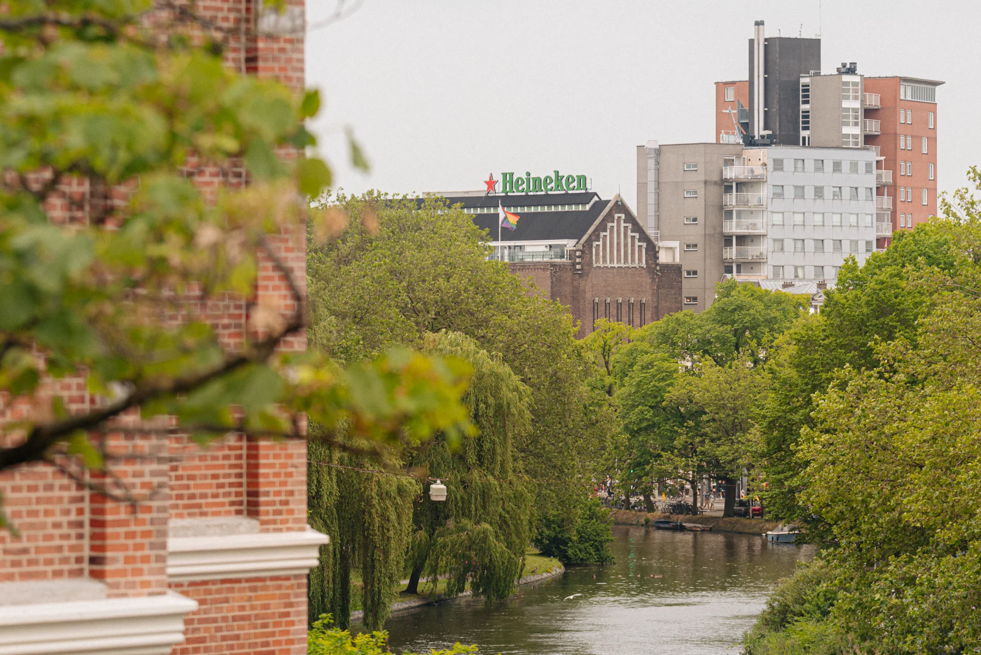 Uitzicht op de Heineken Experience en omliggende gebouwen aan de Weteringschans in Amsterdam, gezien vanaf een groene gracht.