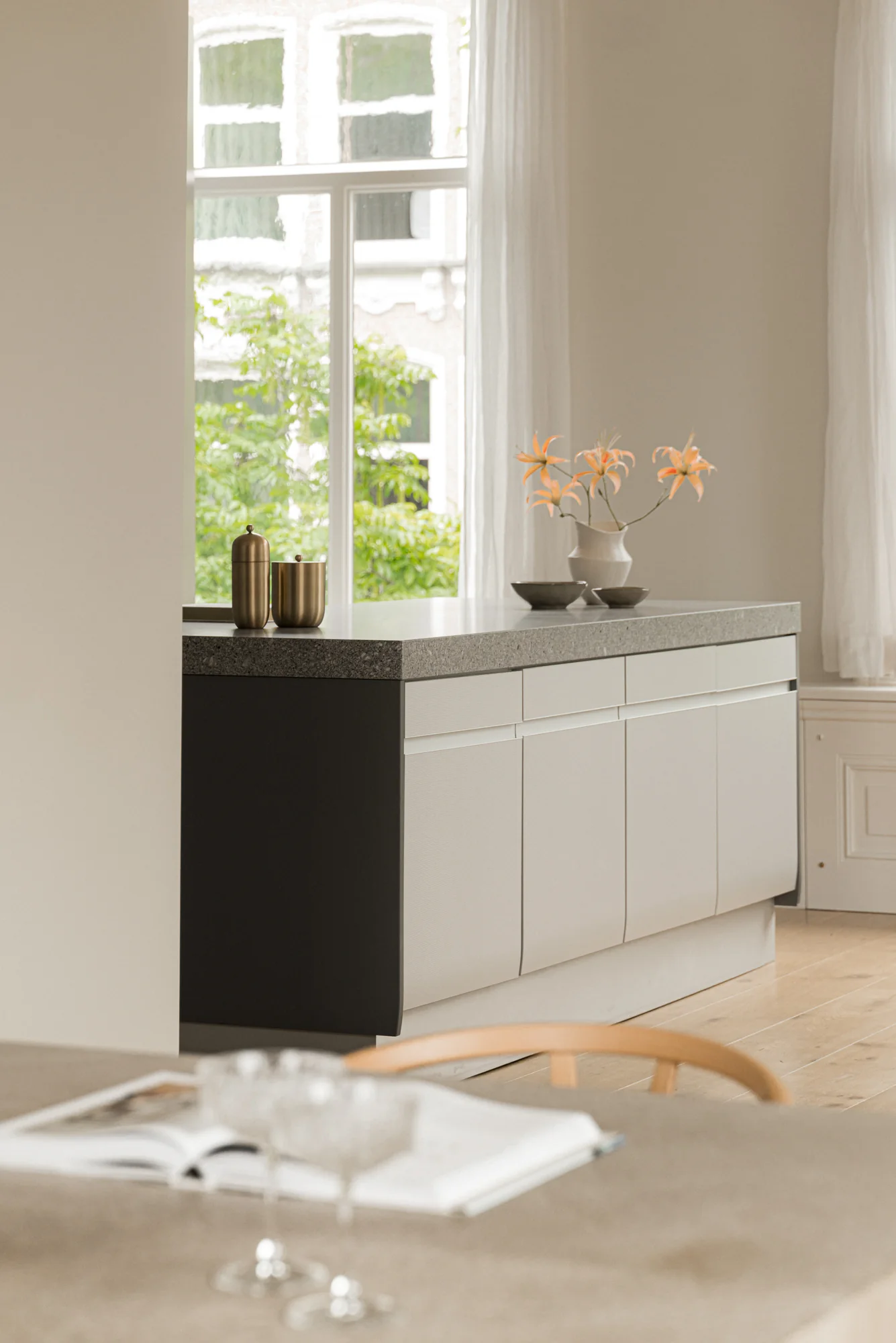 Moderne keukenopstelling aan de Weteringschans met lichtgrijs keukenblok, stenen werkblad en oranje bloemen in een vaas.